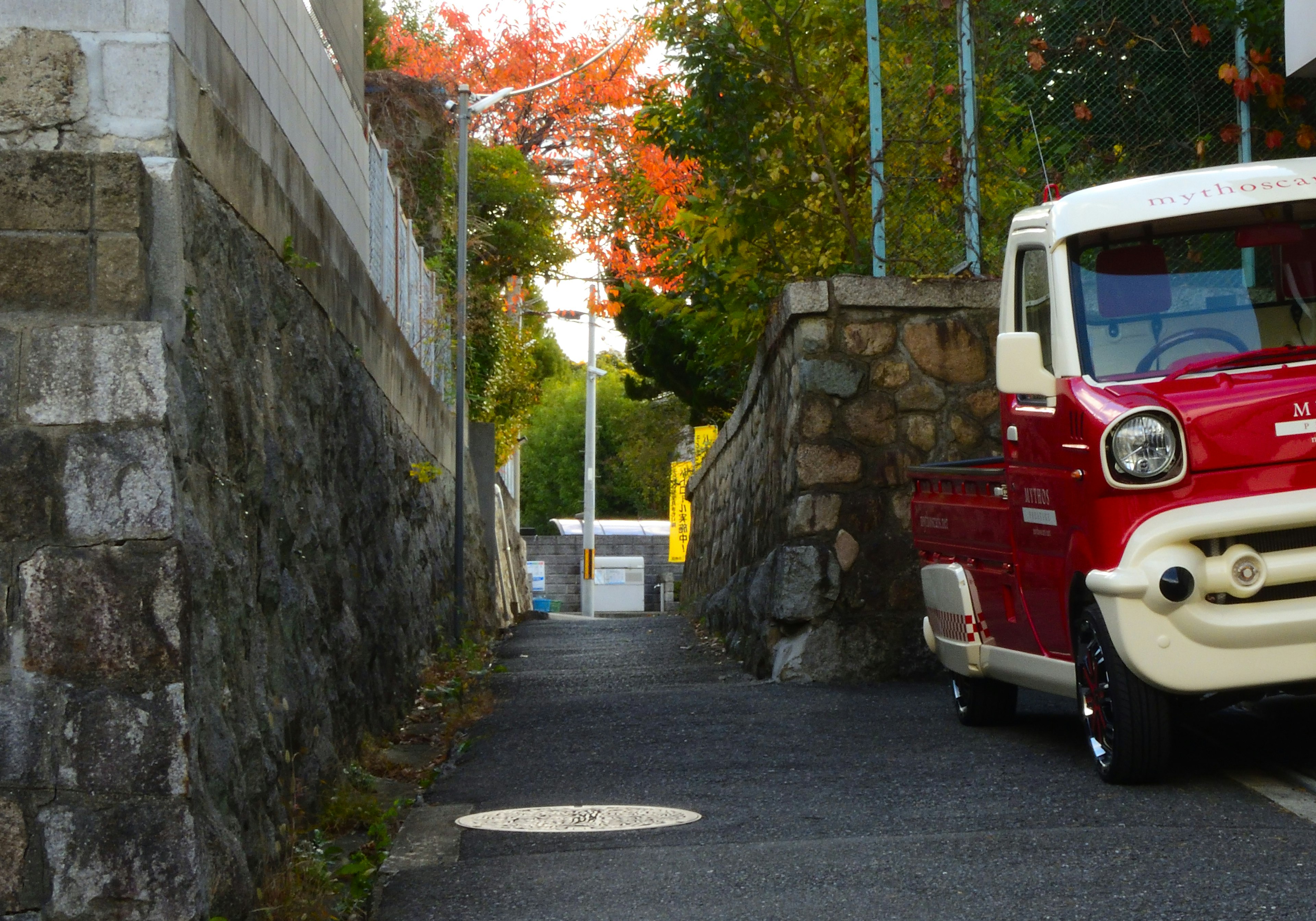 Red truck parked on a narrow street with autumn foliage