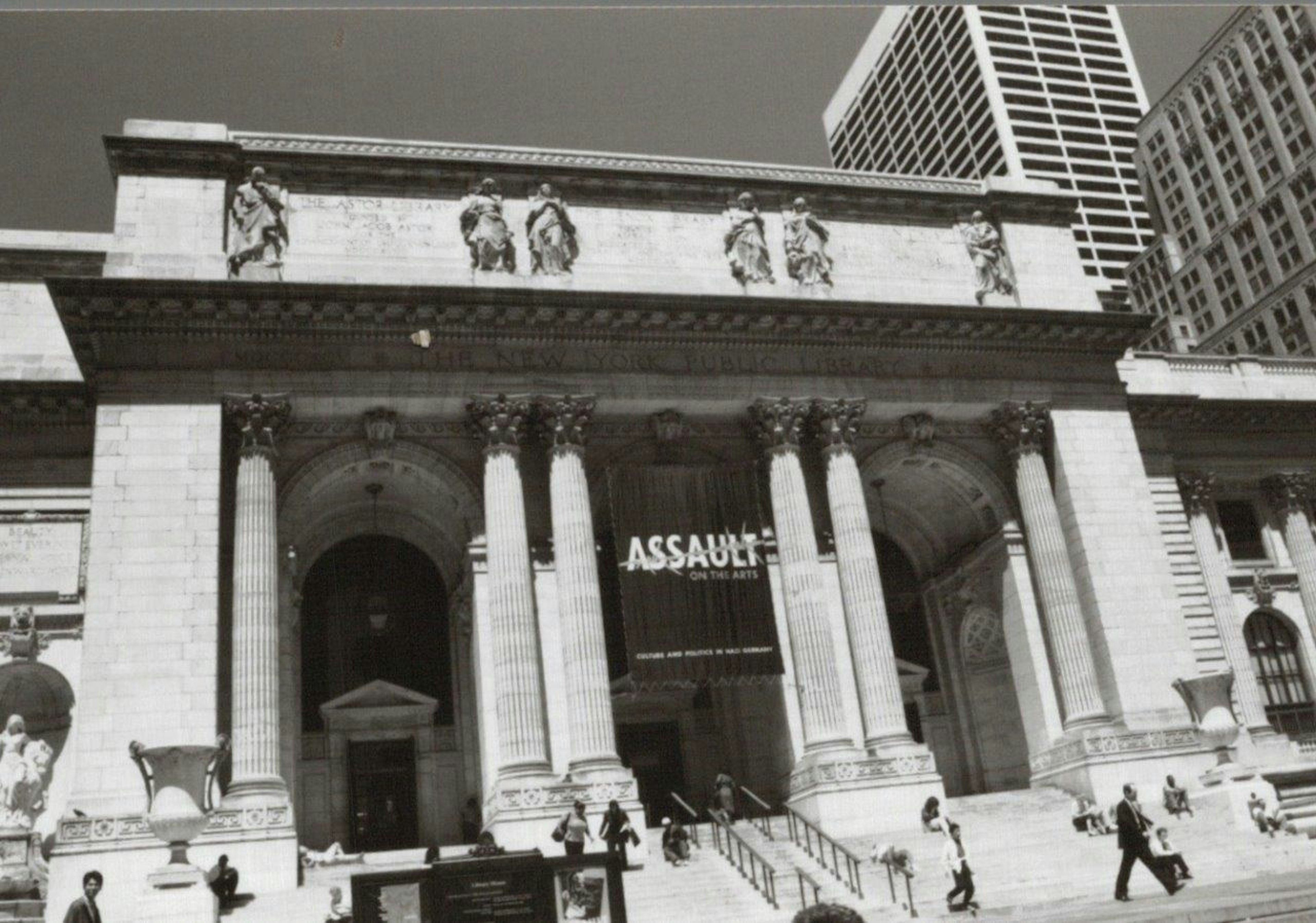 Exterior of New York Public Library featuring grand columns and sculptures prominent ASSAULT sign visible