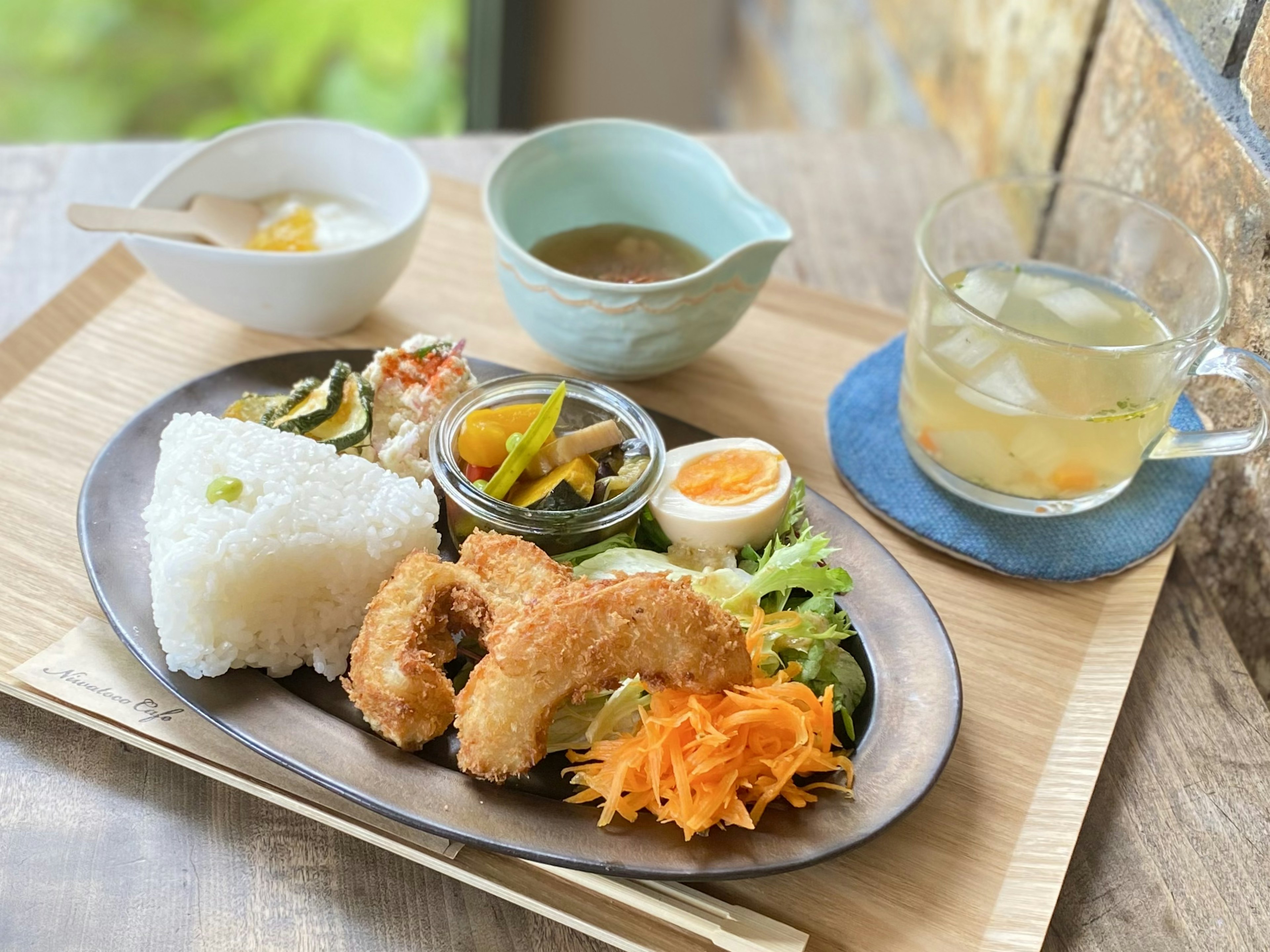 Plate of fried chicken with rice salad soup and drink on a wooden tray