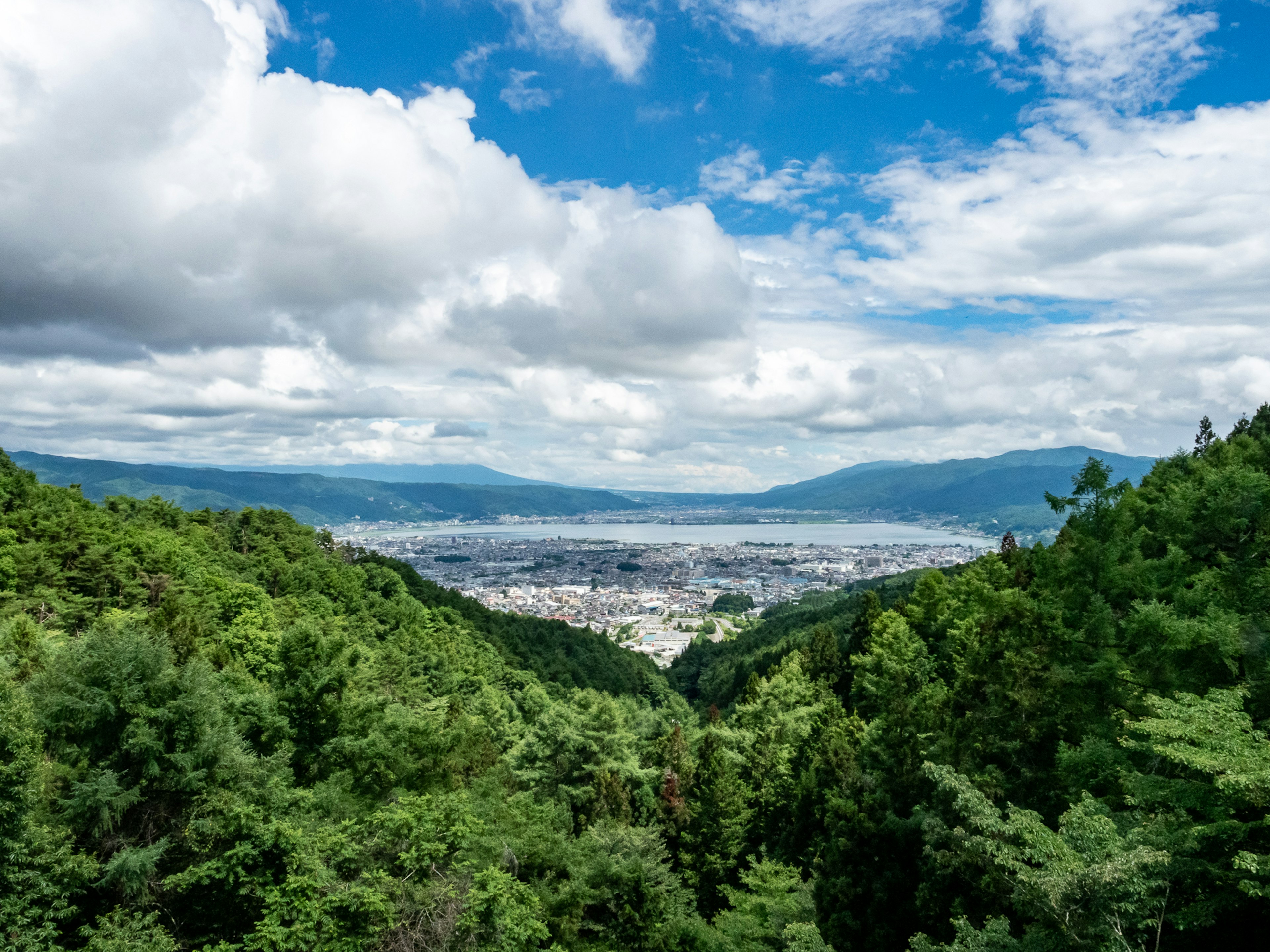 Blick auf eine Stadt umgeben von üppigen grünen Bergen und blauem Himmel