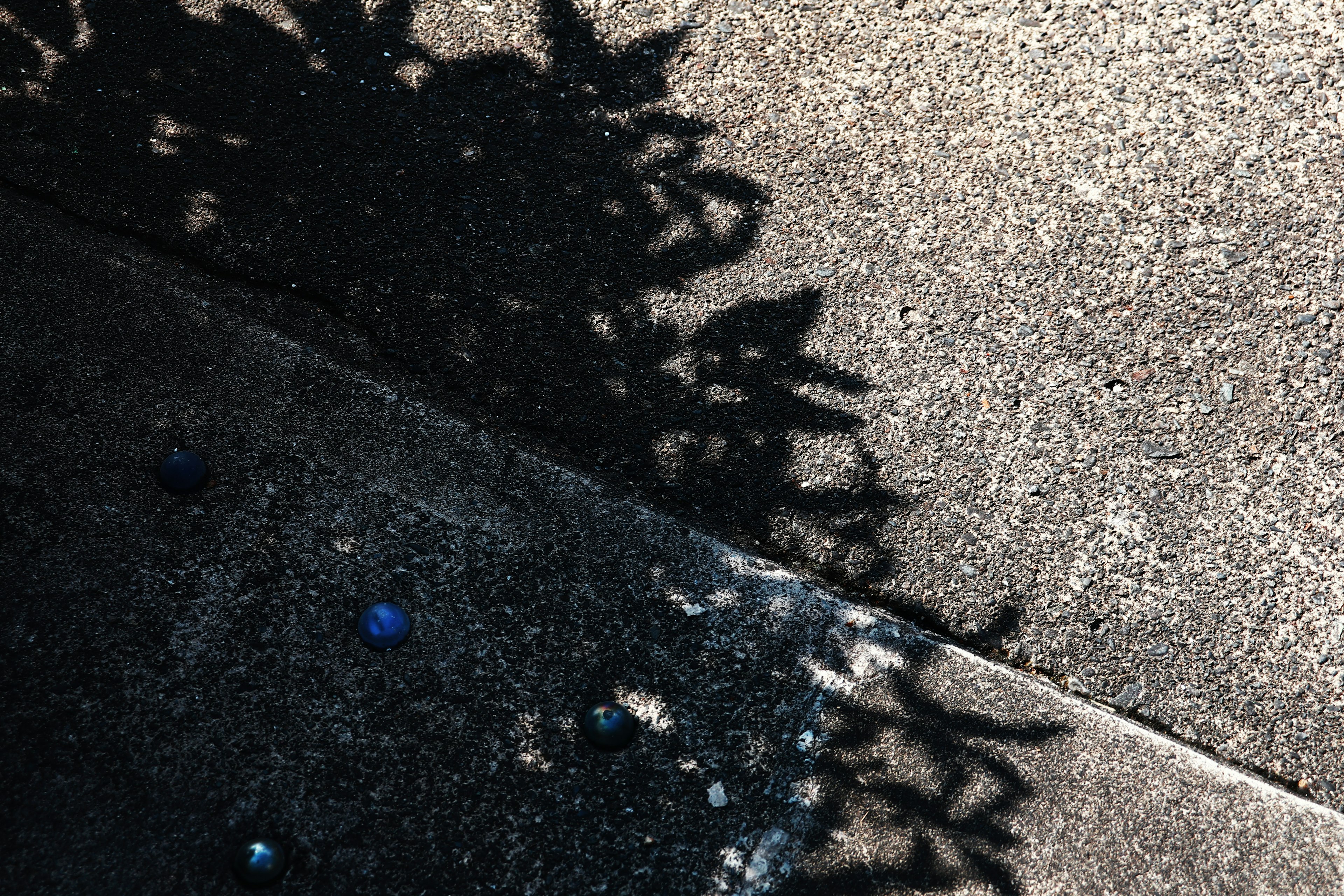 A shadow cast on concrete with colorful beads scattered on the surface