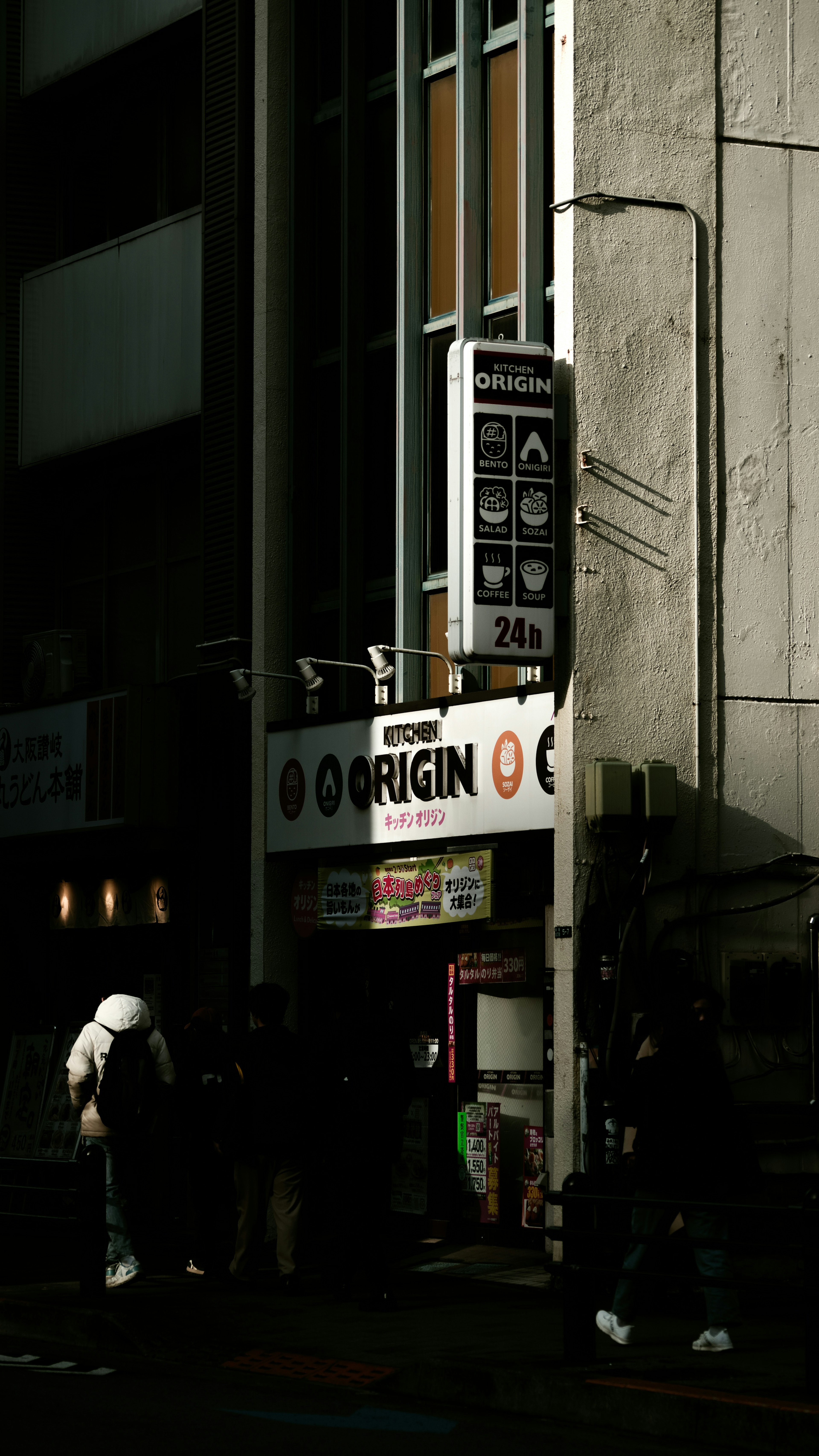 暗い街角にあるORIGINの看板と人々の姿