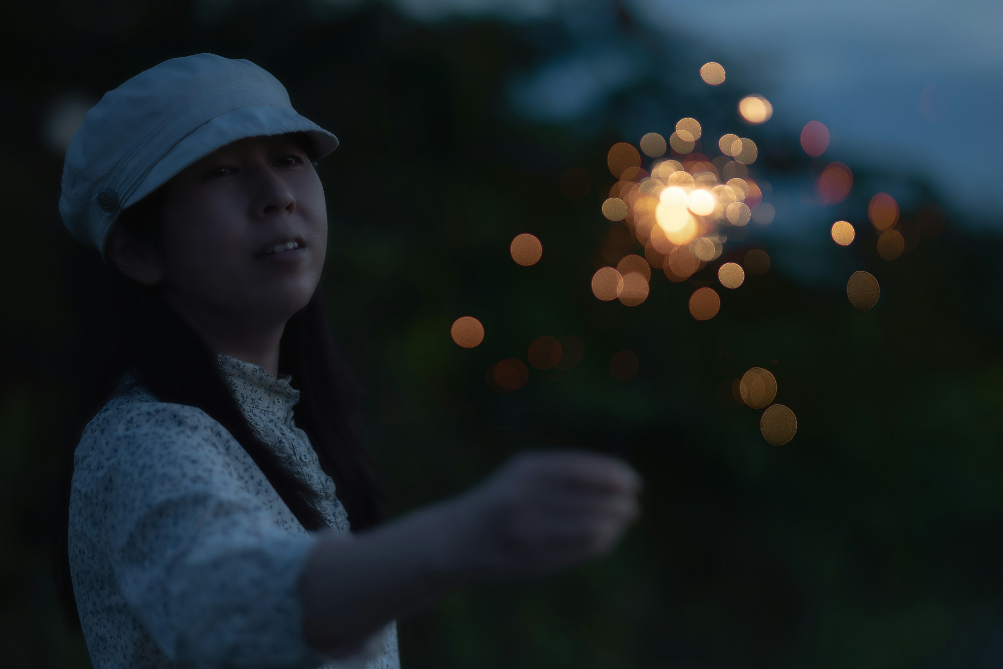 Una niña sosteniendo un fuego artificial con luces borrosas de fondo al anochecer