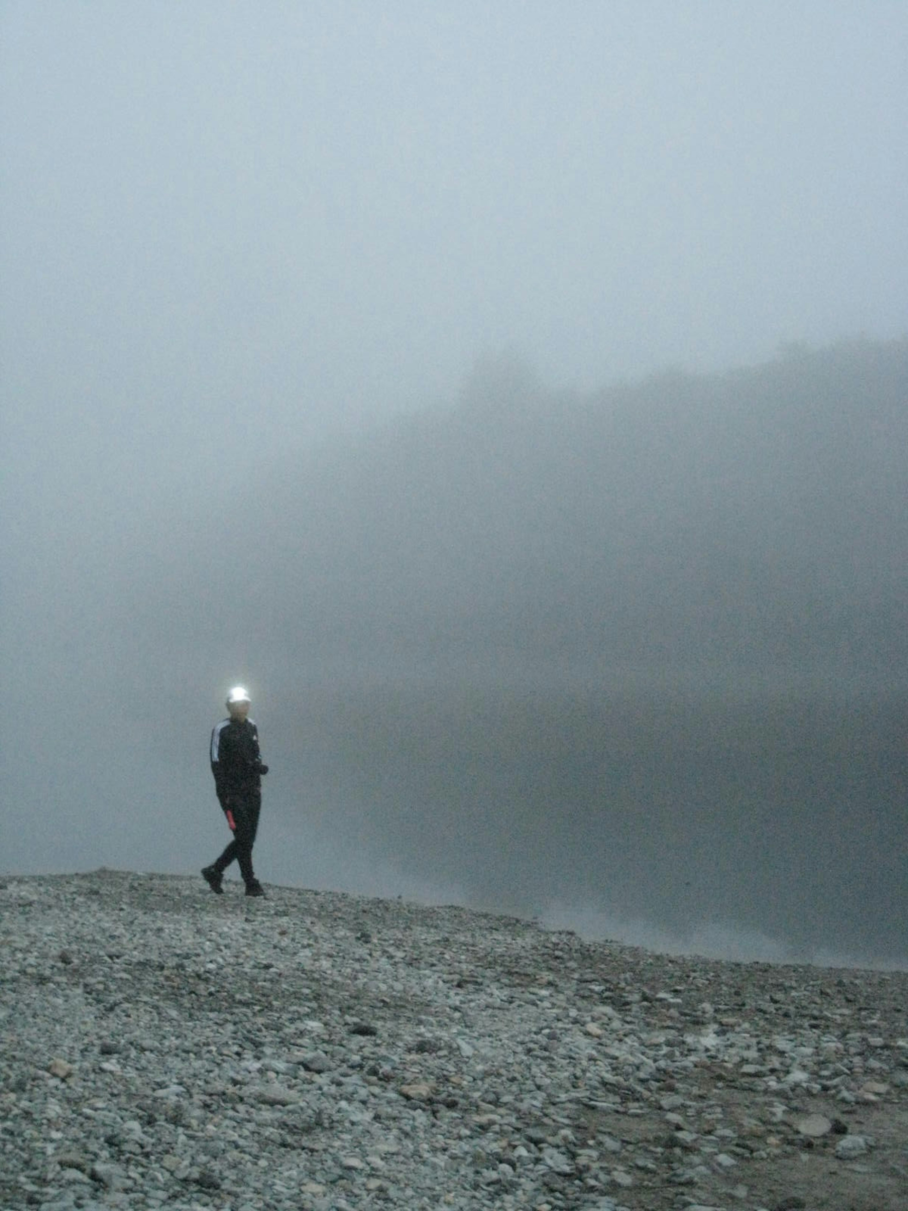 Person walking in fog near a calm lake