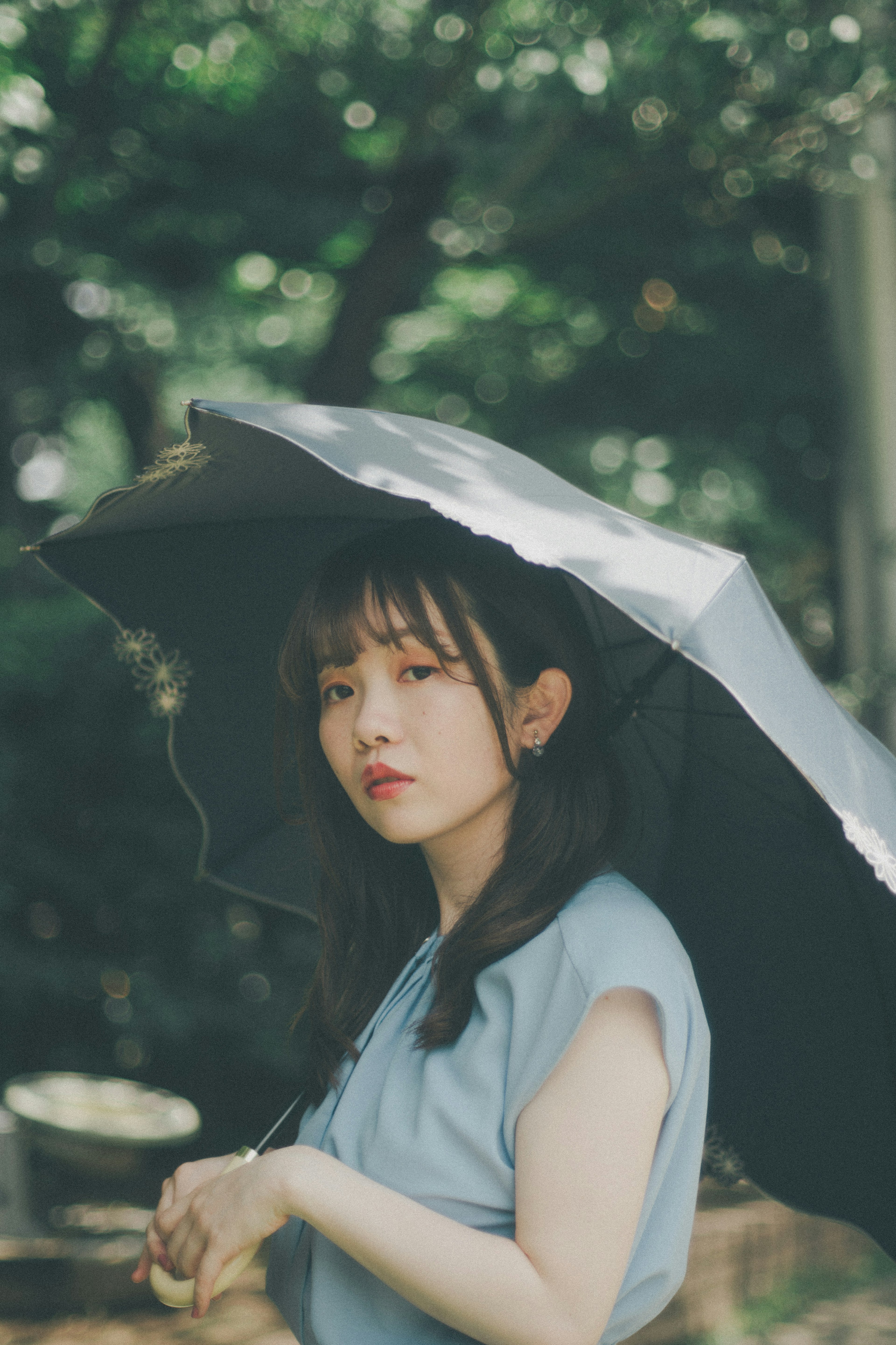 Un retrato de una mujer sosteniendo un parasol con árboles verdes de fondo