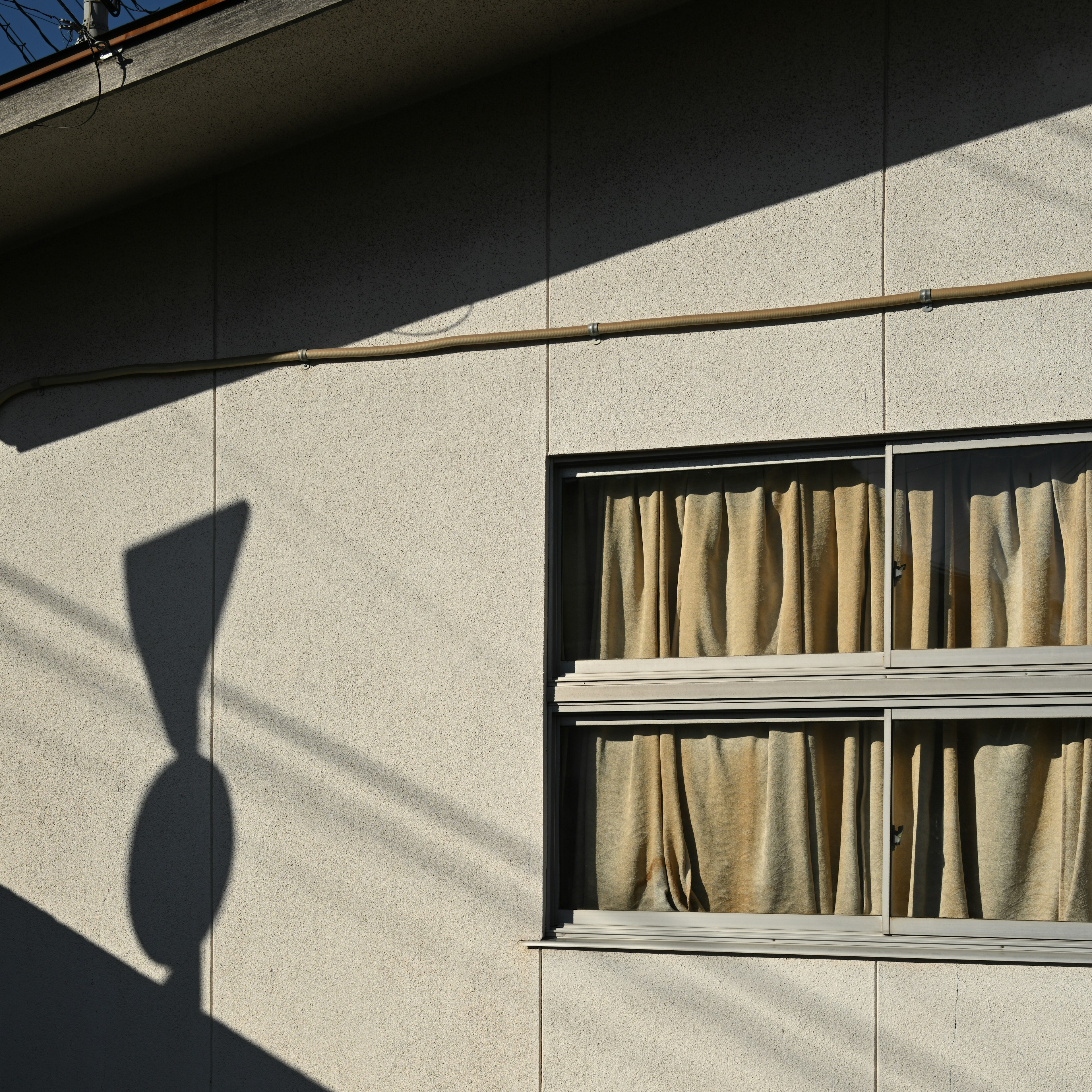 Muro illuminato dal sole con una finestra e tende che creano un'ombra