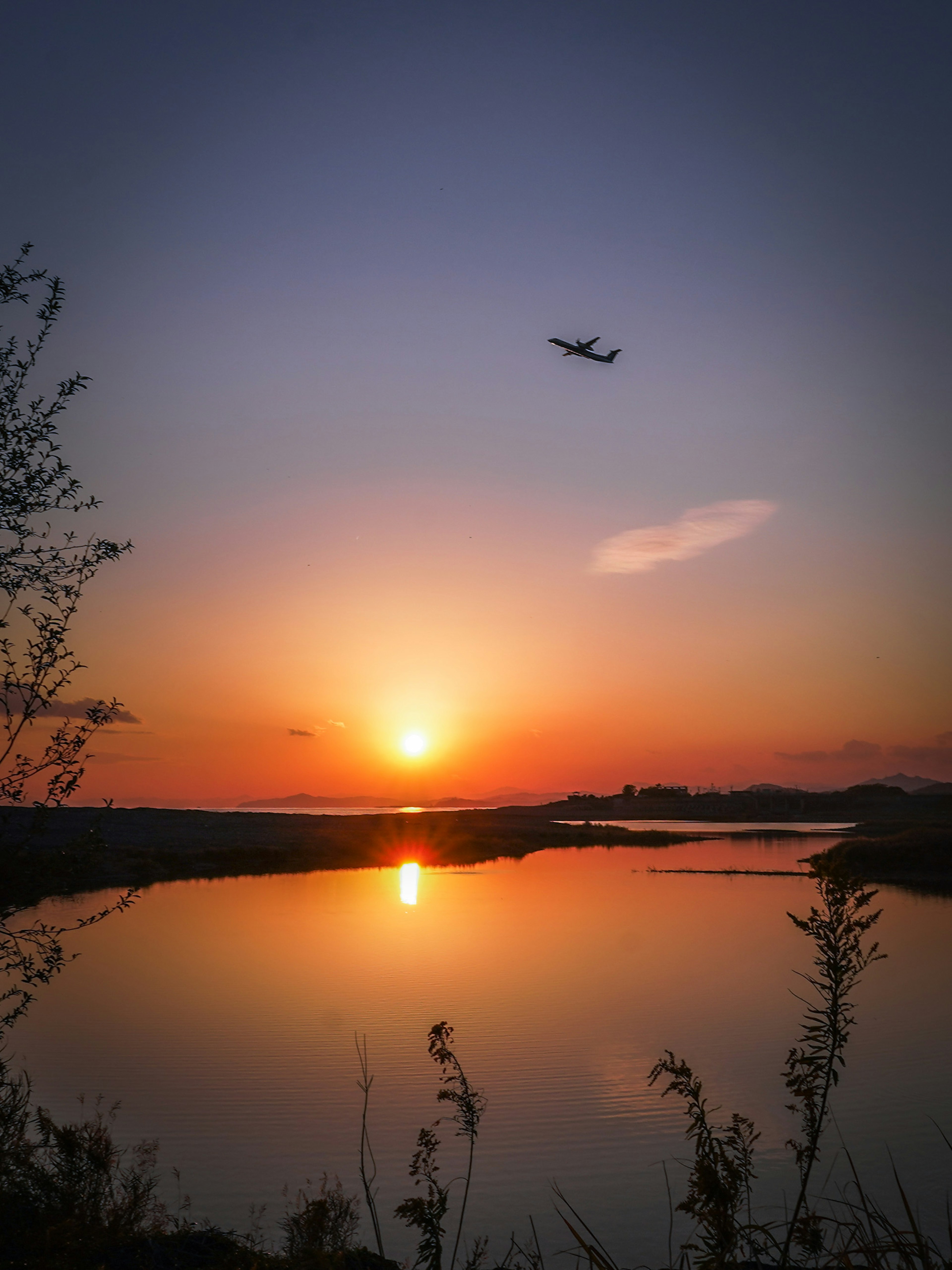 夕日が沈む川の上を飛ぶ飛行機