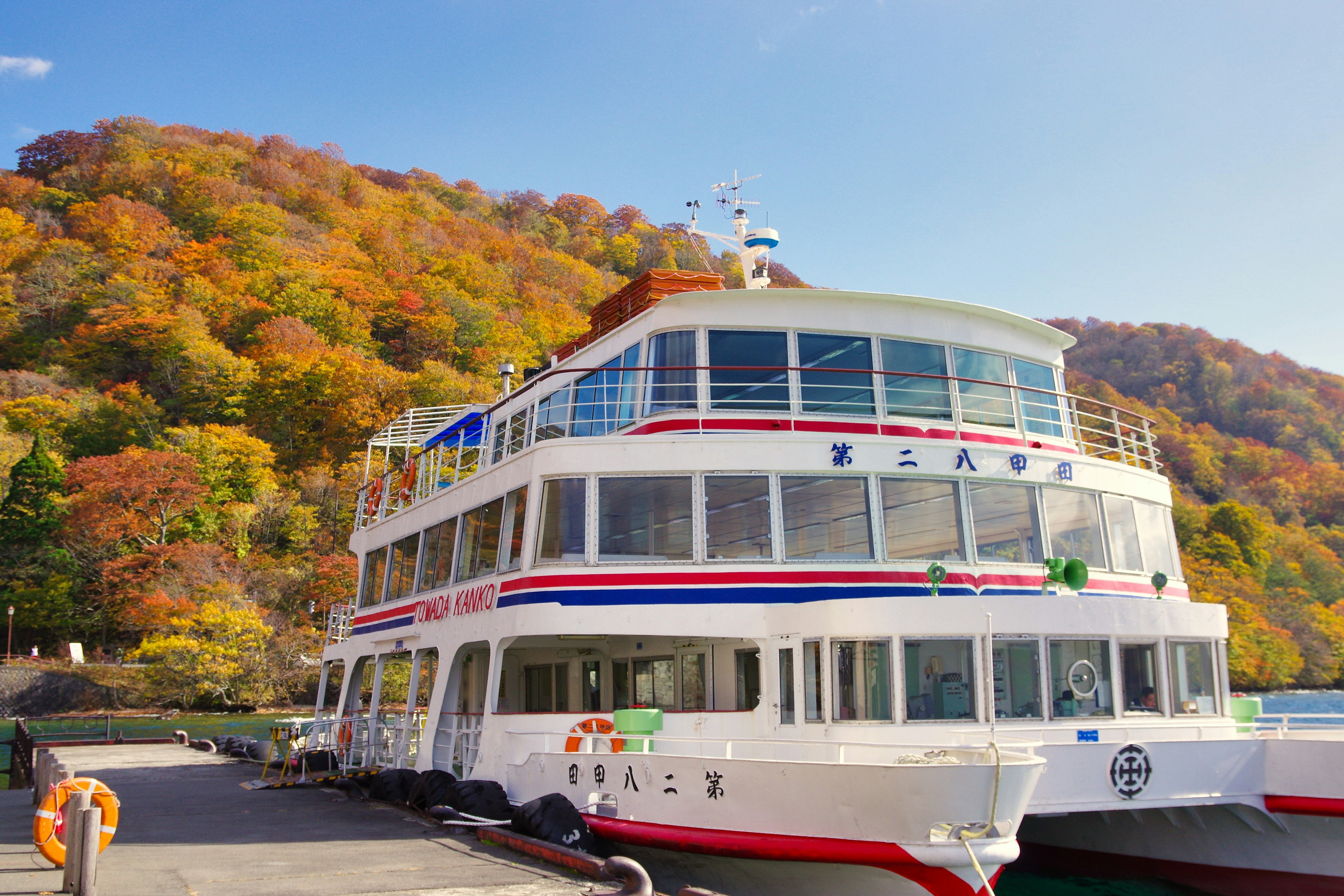 Ein Touristenboot im Hafen mit bunten Herbstblättern im Hintergrund