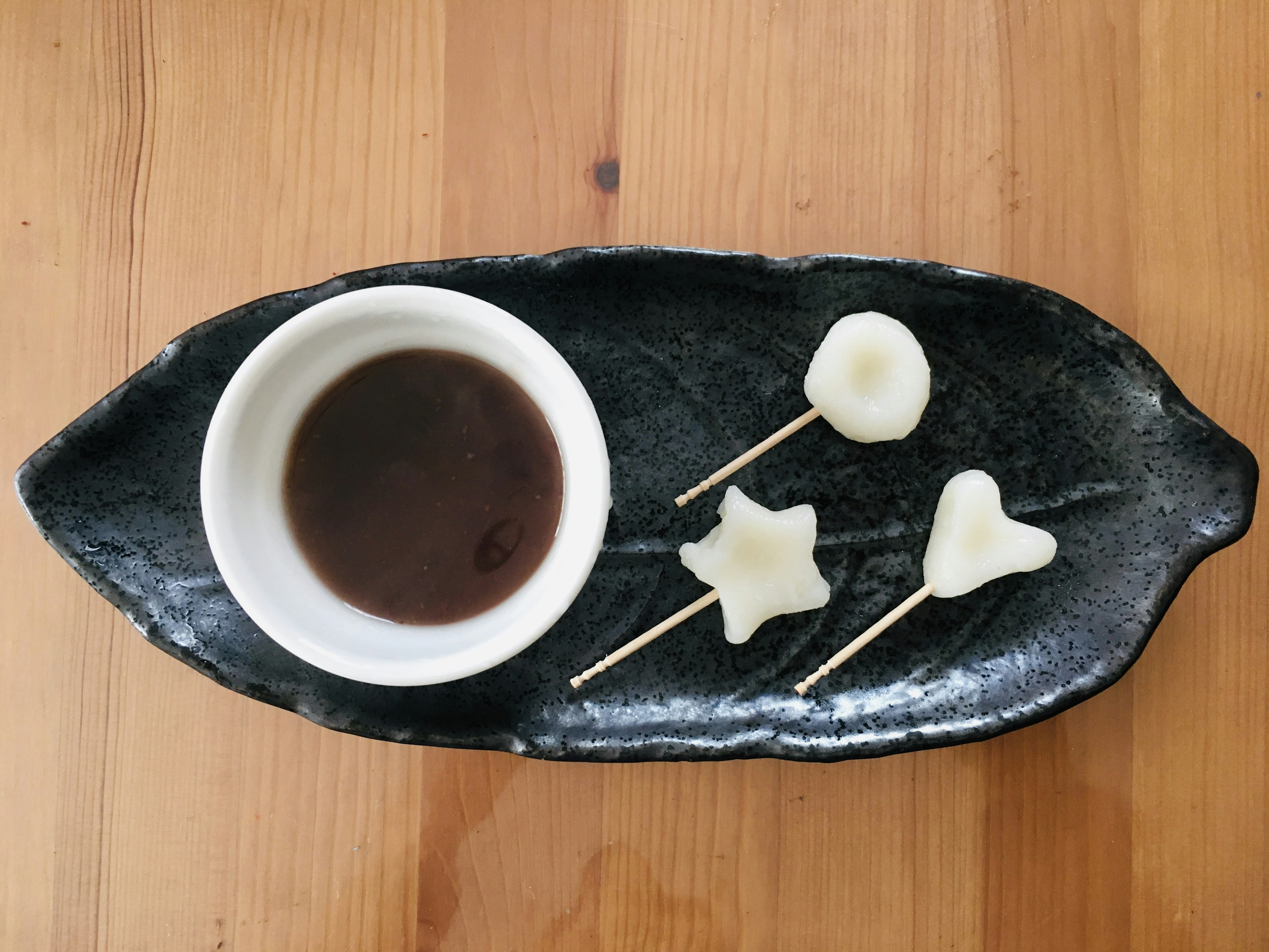 White sweets shaped like stars and circles served with dipping sauce on a black plate