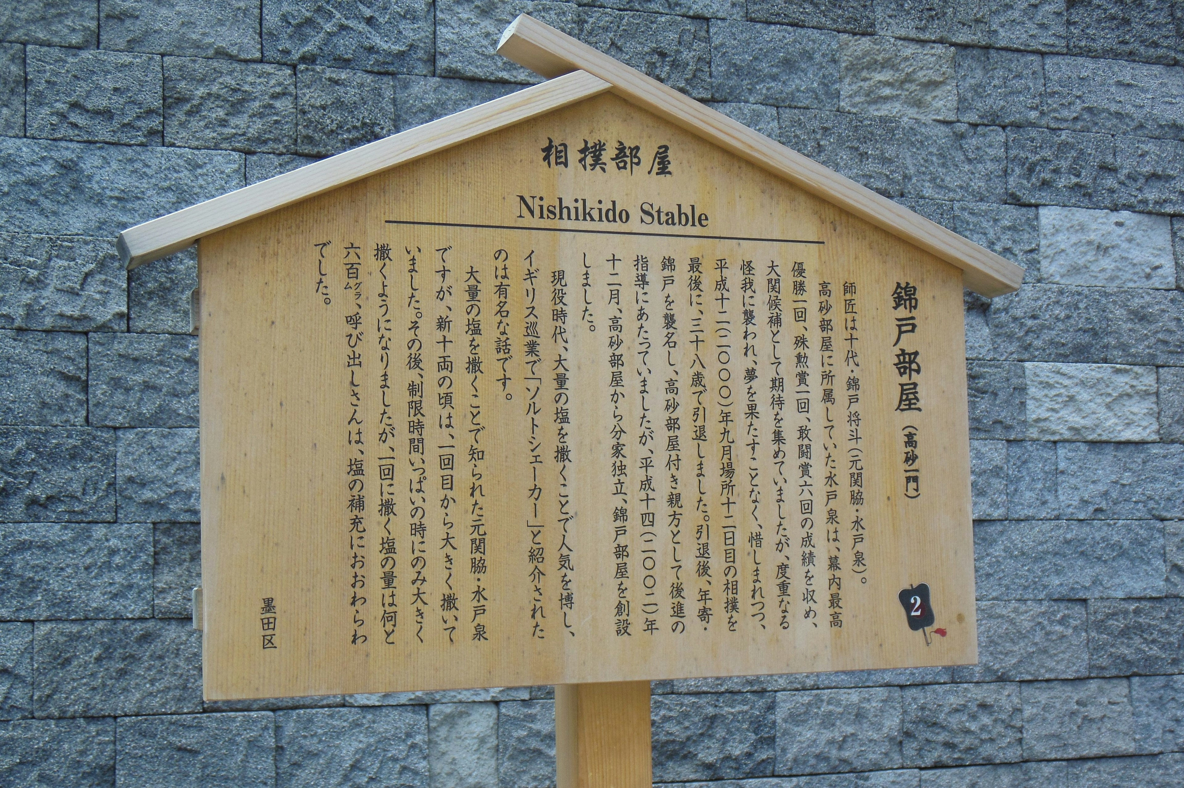 Cartel de madera frente a una pared de piedra que presenta un texto sobre la cultura japonesa