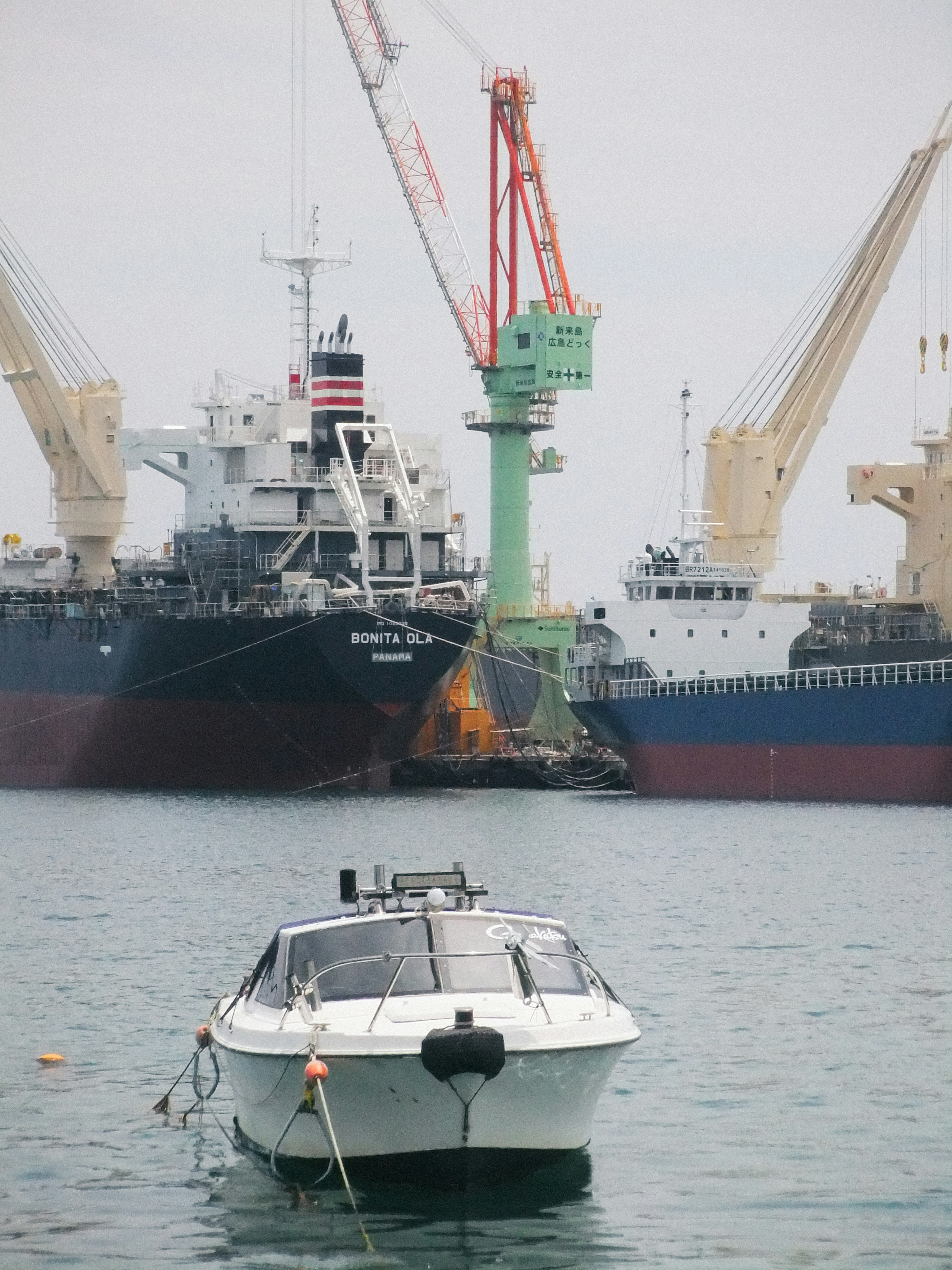 A small boat anchored in a port with large cargo ships in the background