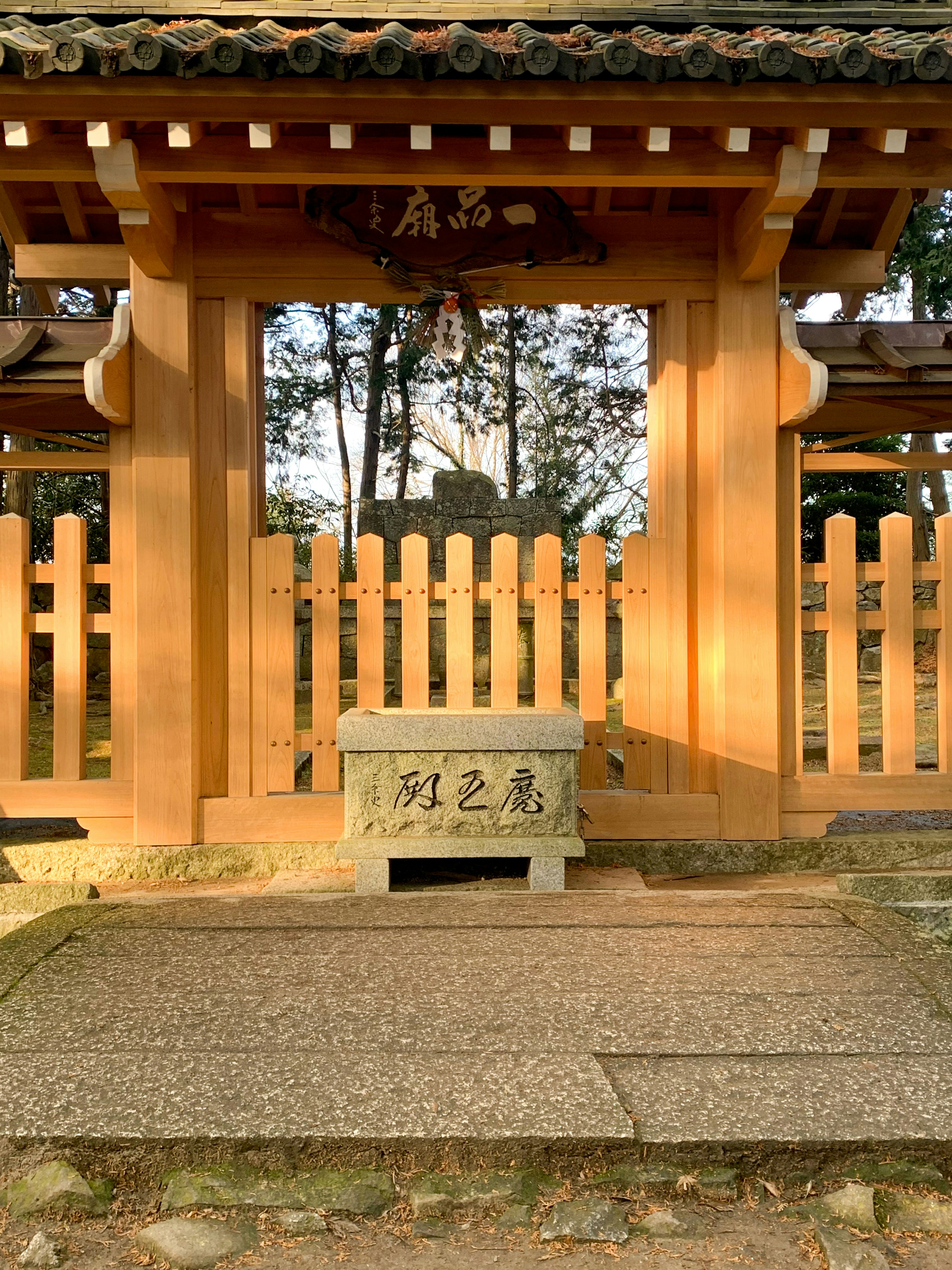 Entrada de un santuario japonés con puerta de madera y pedestal de piedra