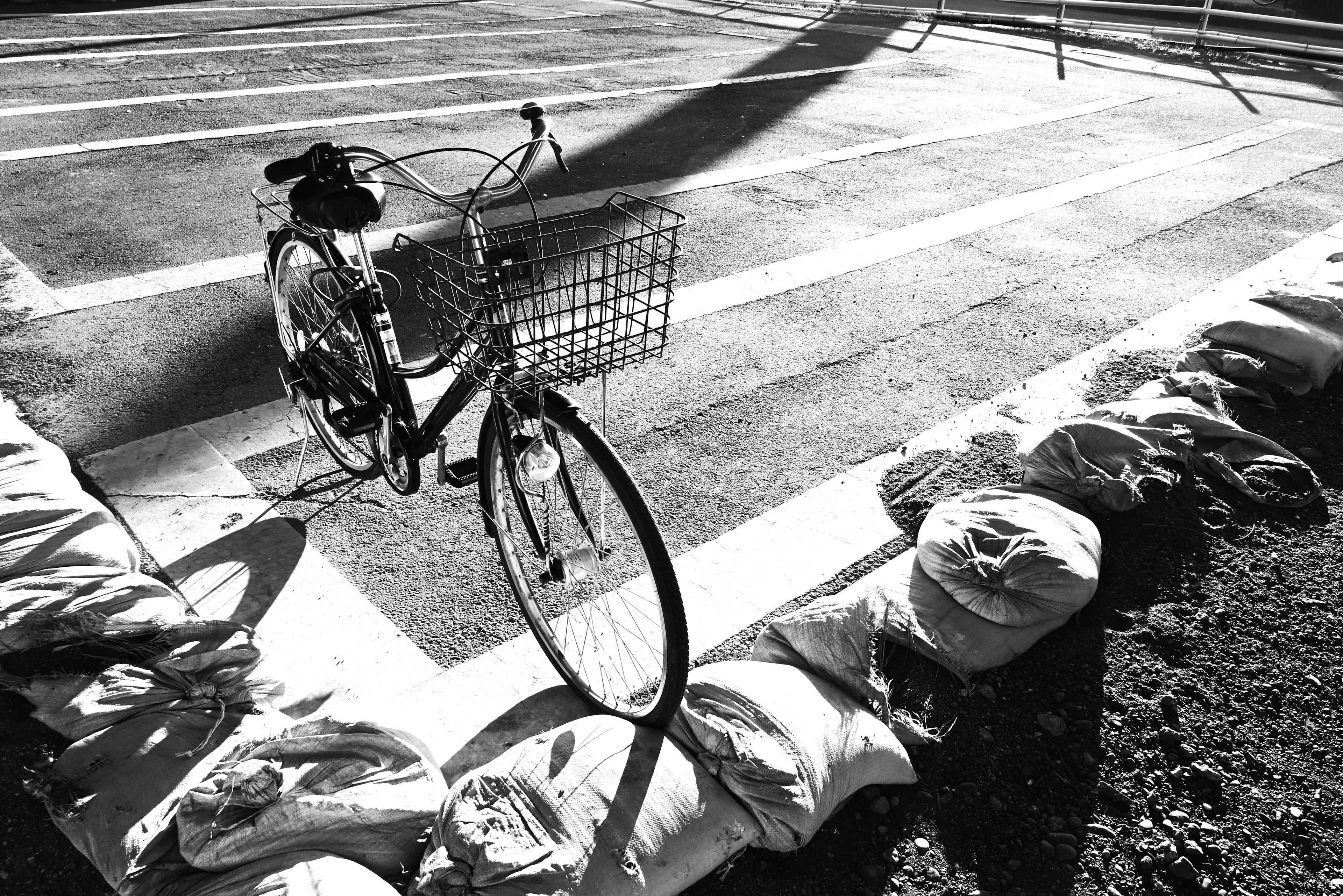 Image en noir et blanc d'un vélo à côté de sacs de sable sur une route