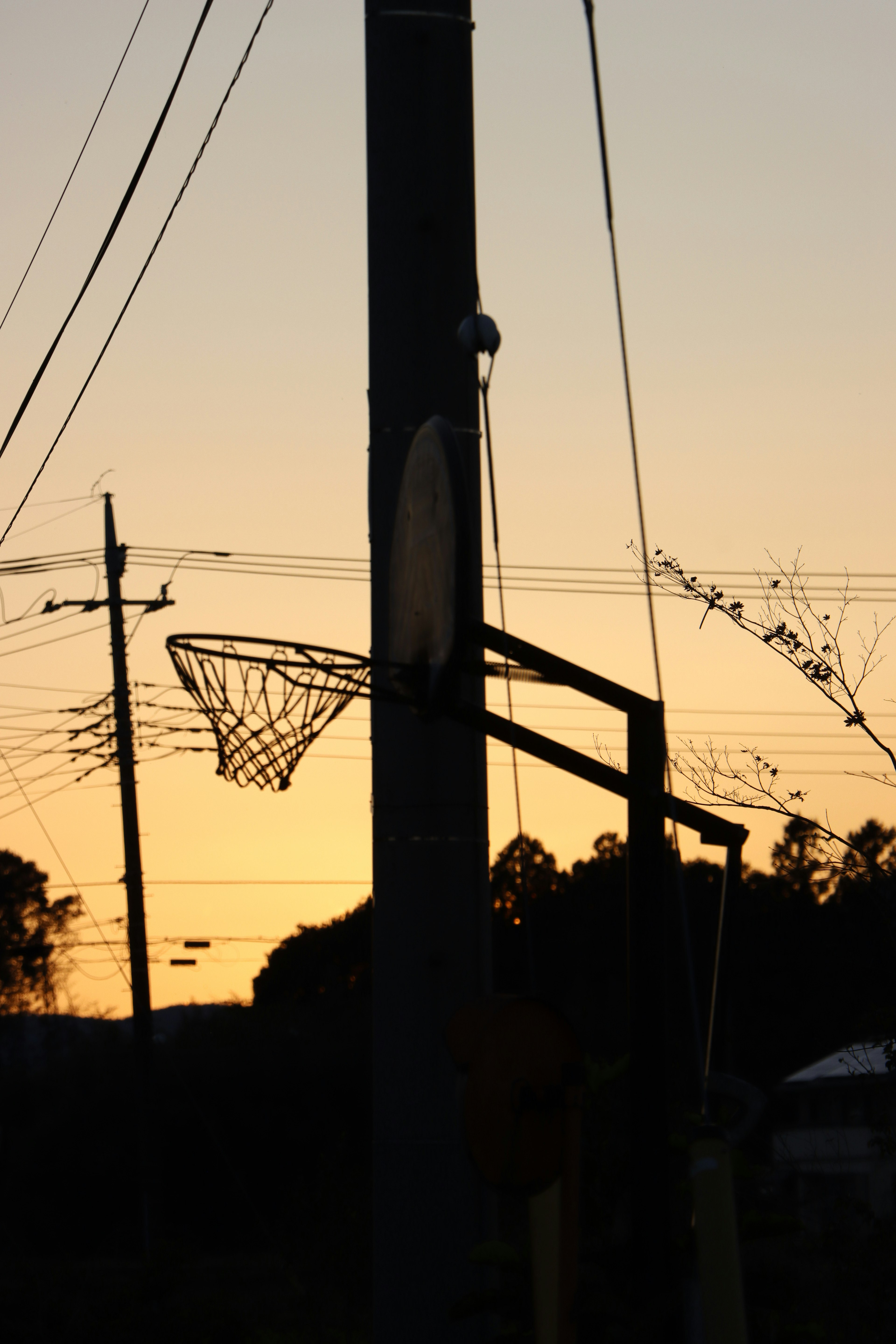 Siluet ring basket dan tiang listrik melawan langit senja