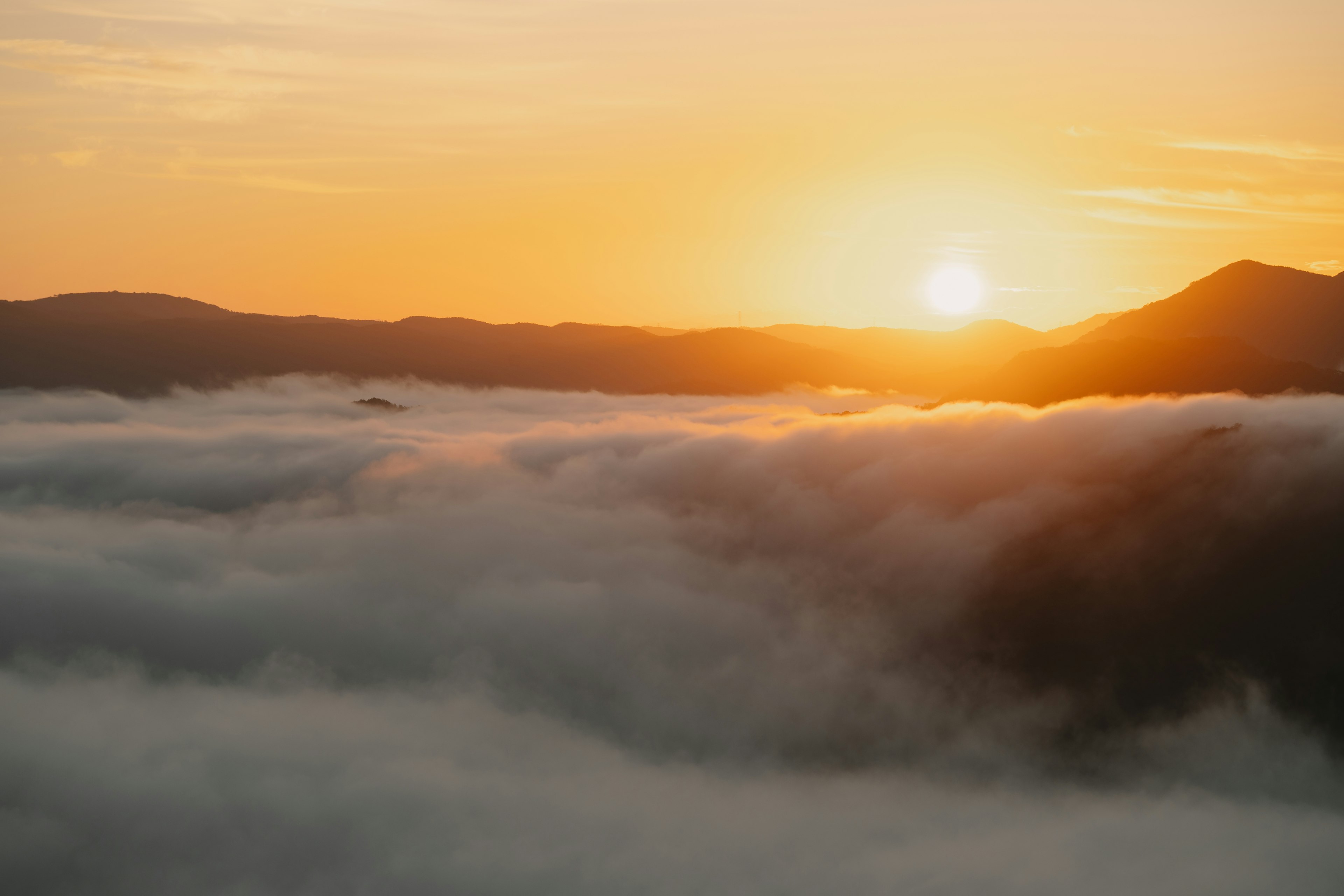 Orange sun rising above clouds silhouettes of mountains in the background