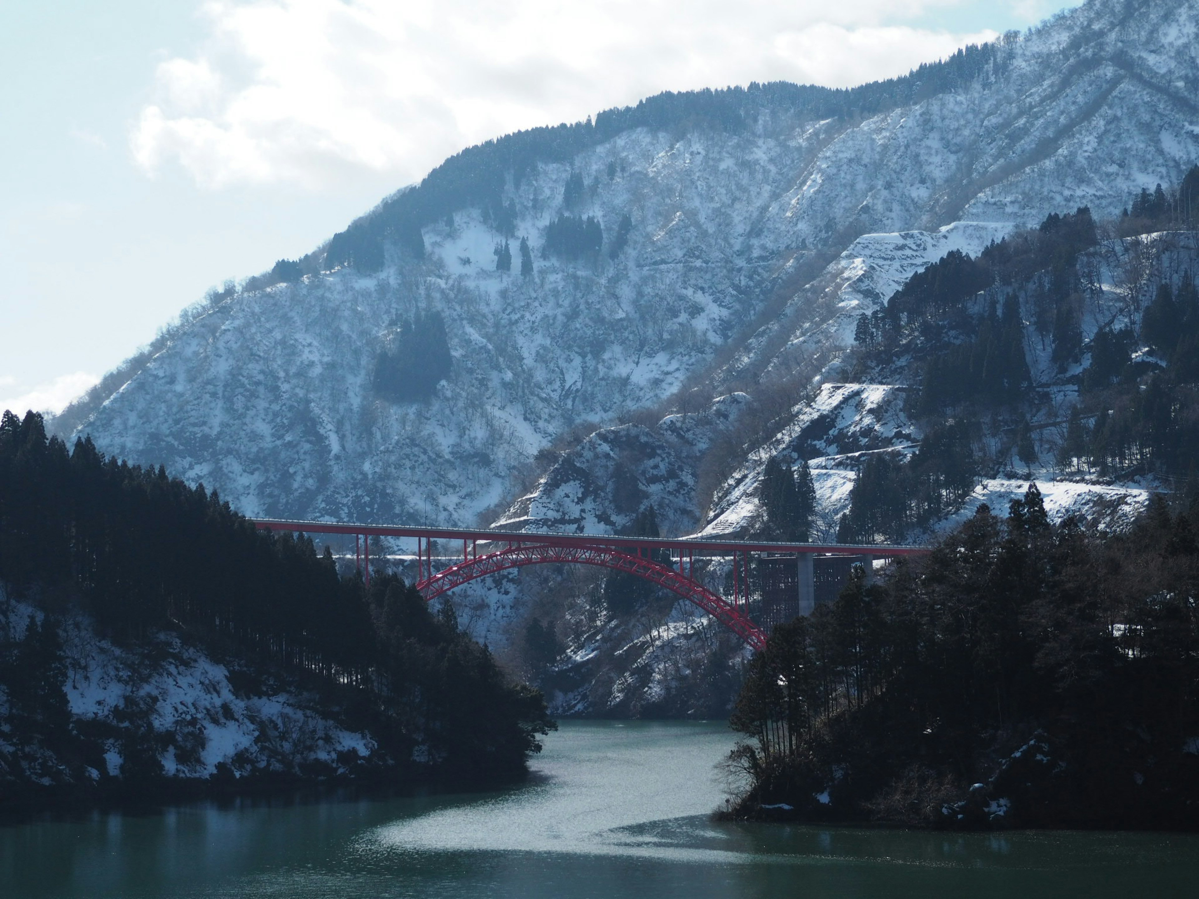 Red bridge spanning a river surrounded by snow-covered mountains