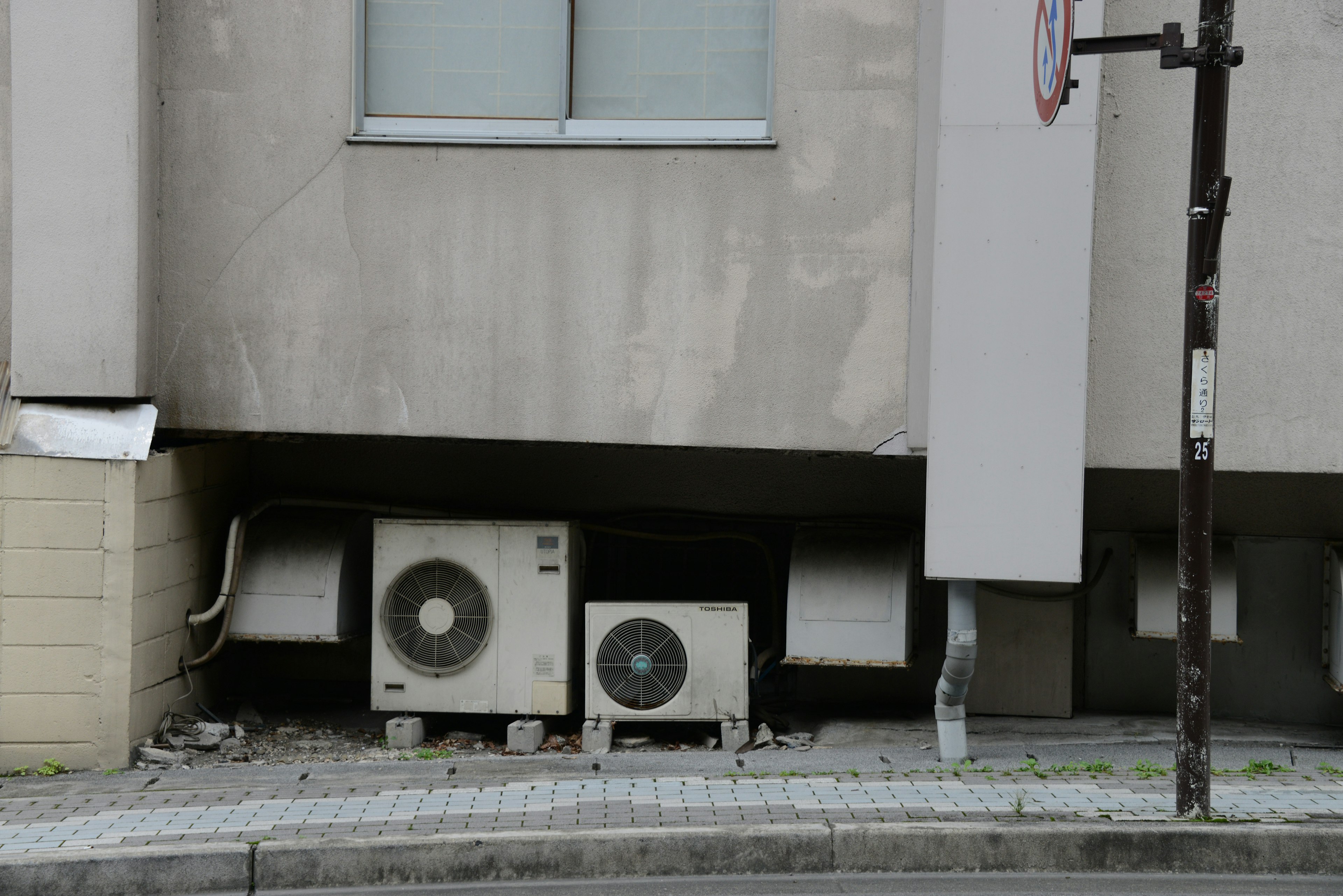 Two air conditioning units installed on the exterior wall of a building with surrounding pavement