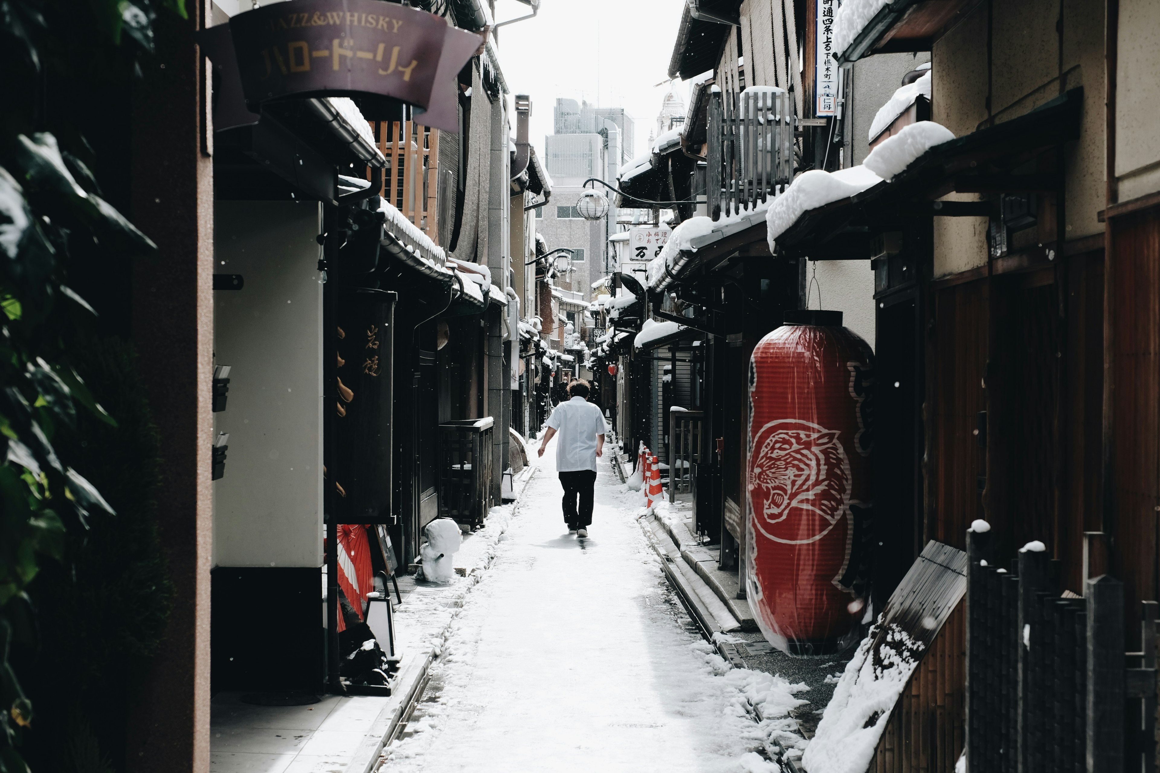 A person walking down a narrow snow-covered alley with traditional buildings