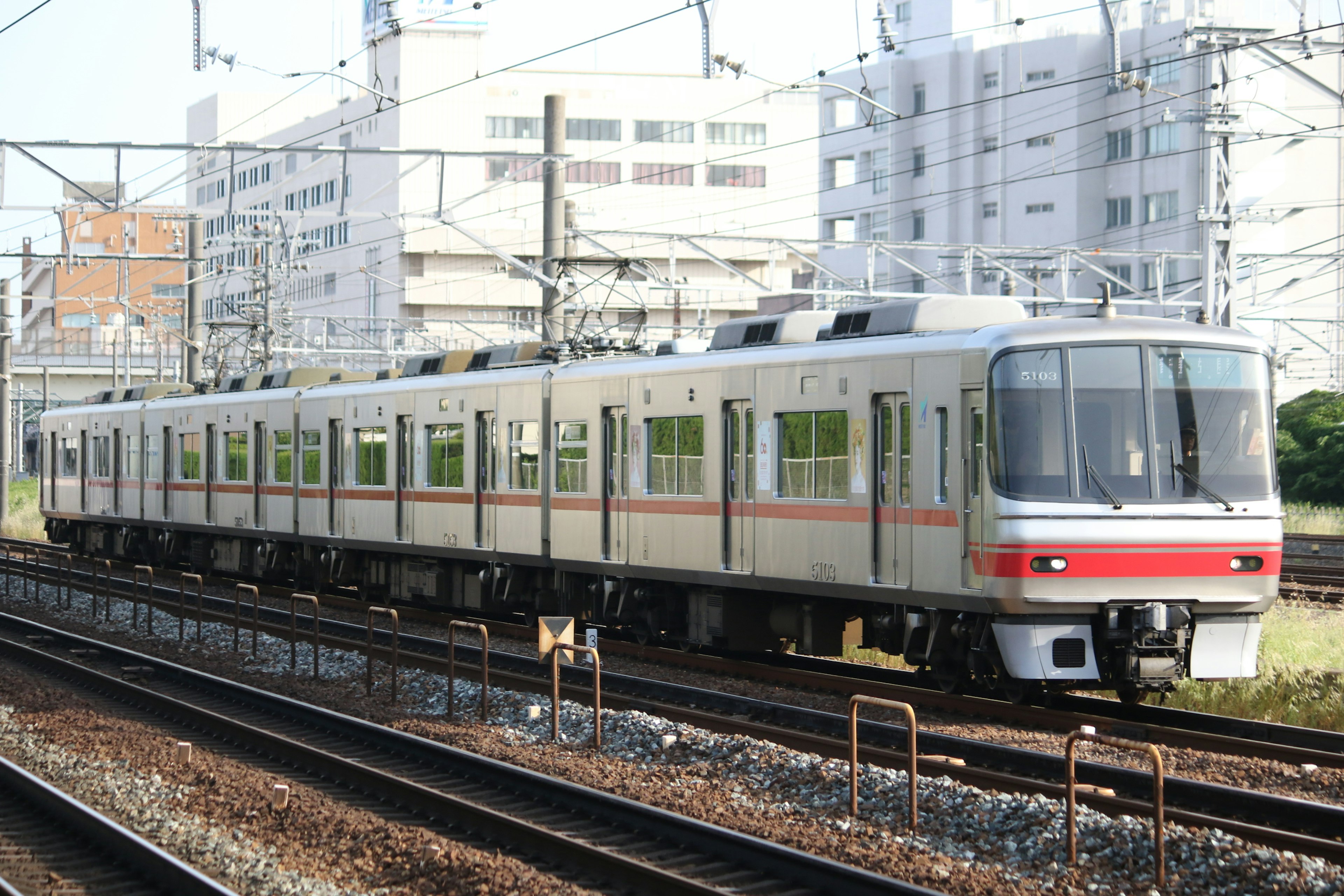 A Japanese train running on tracks with modern buildings in the background