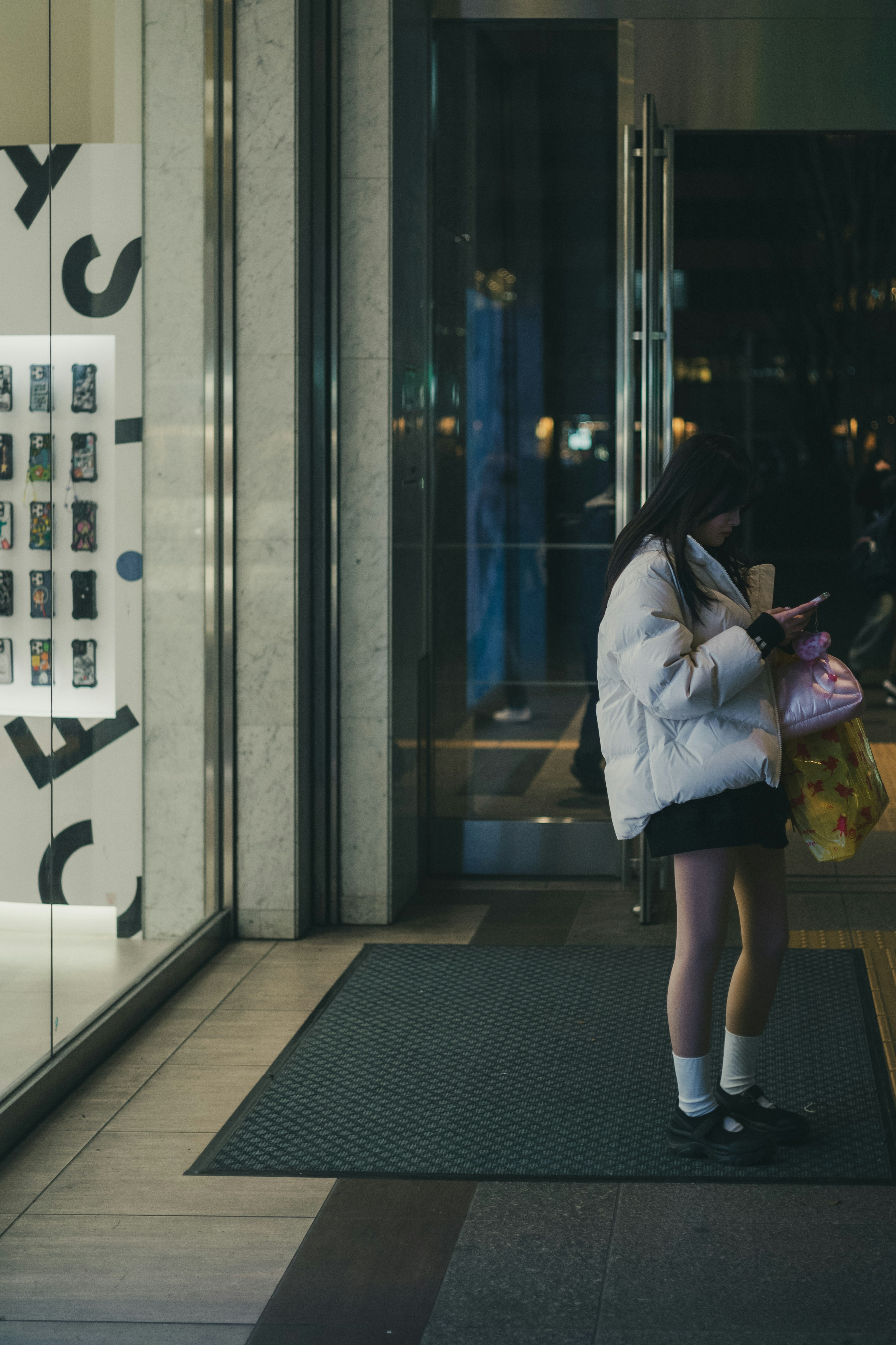 Une fille en veste blanche se tient devant l'entrée d'un magasin