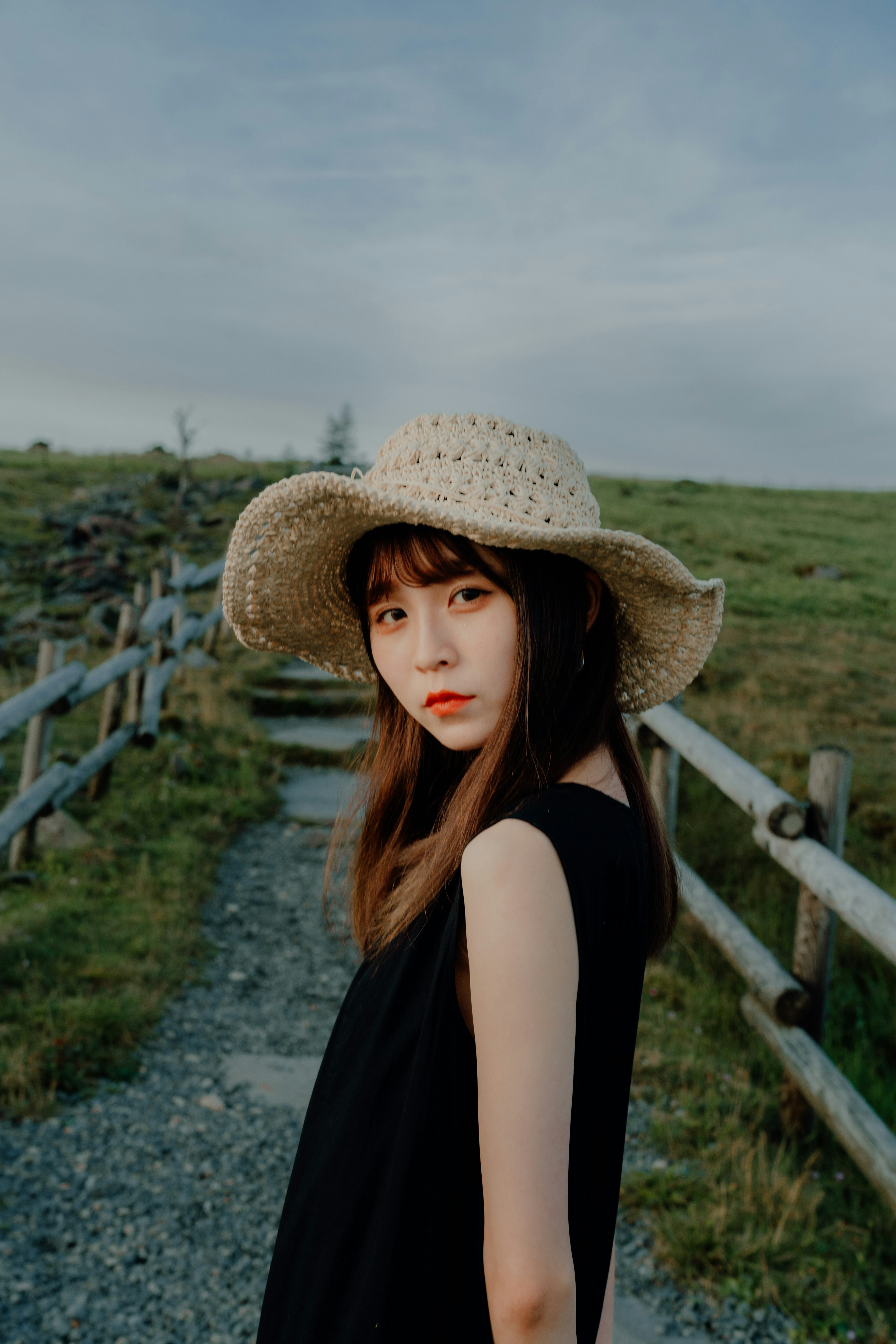 Portrait of a woman turning on a grassy path wearing a straw hat and a black dress