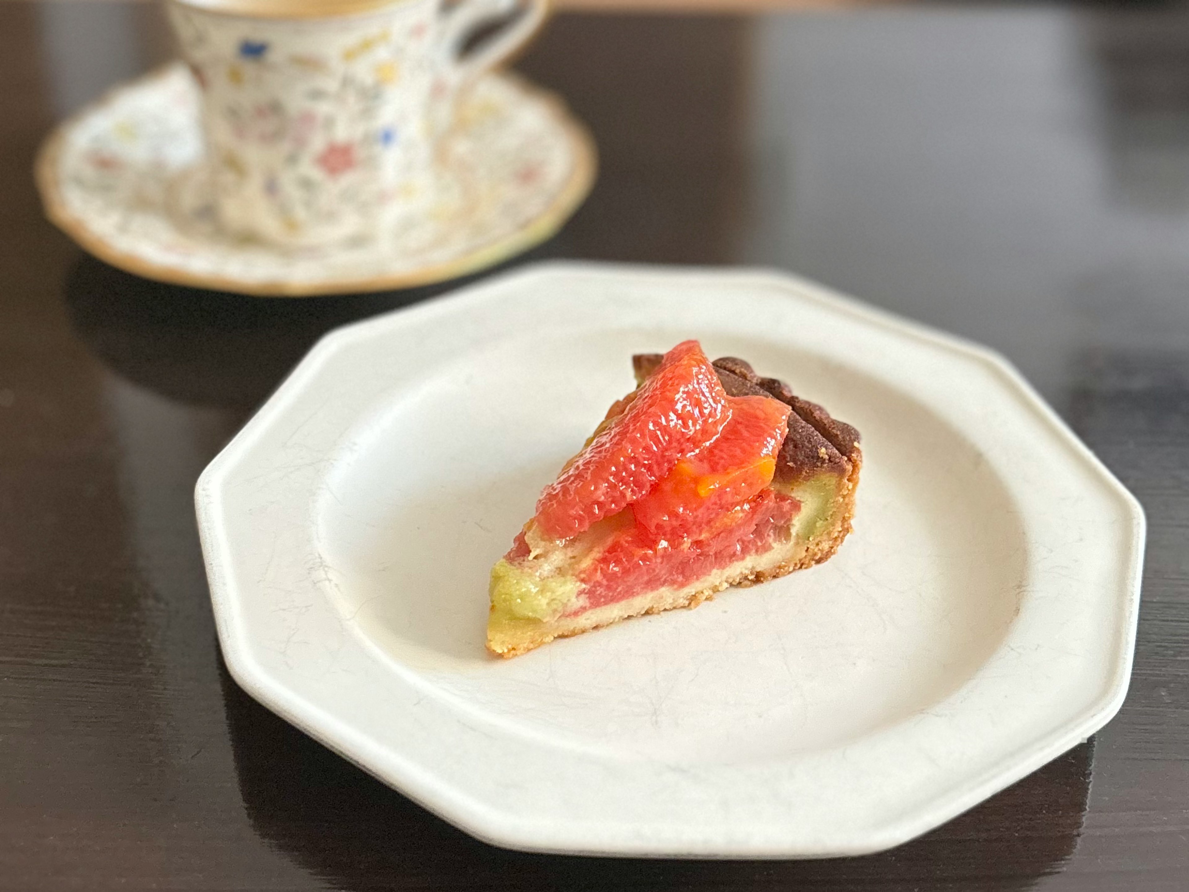 Slice of grapefruit tart on a white plate with a cup of tea in the background