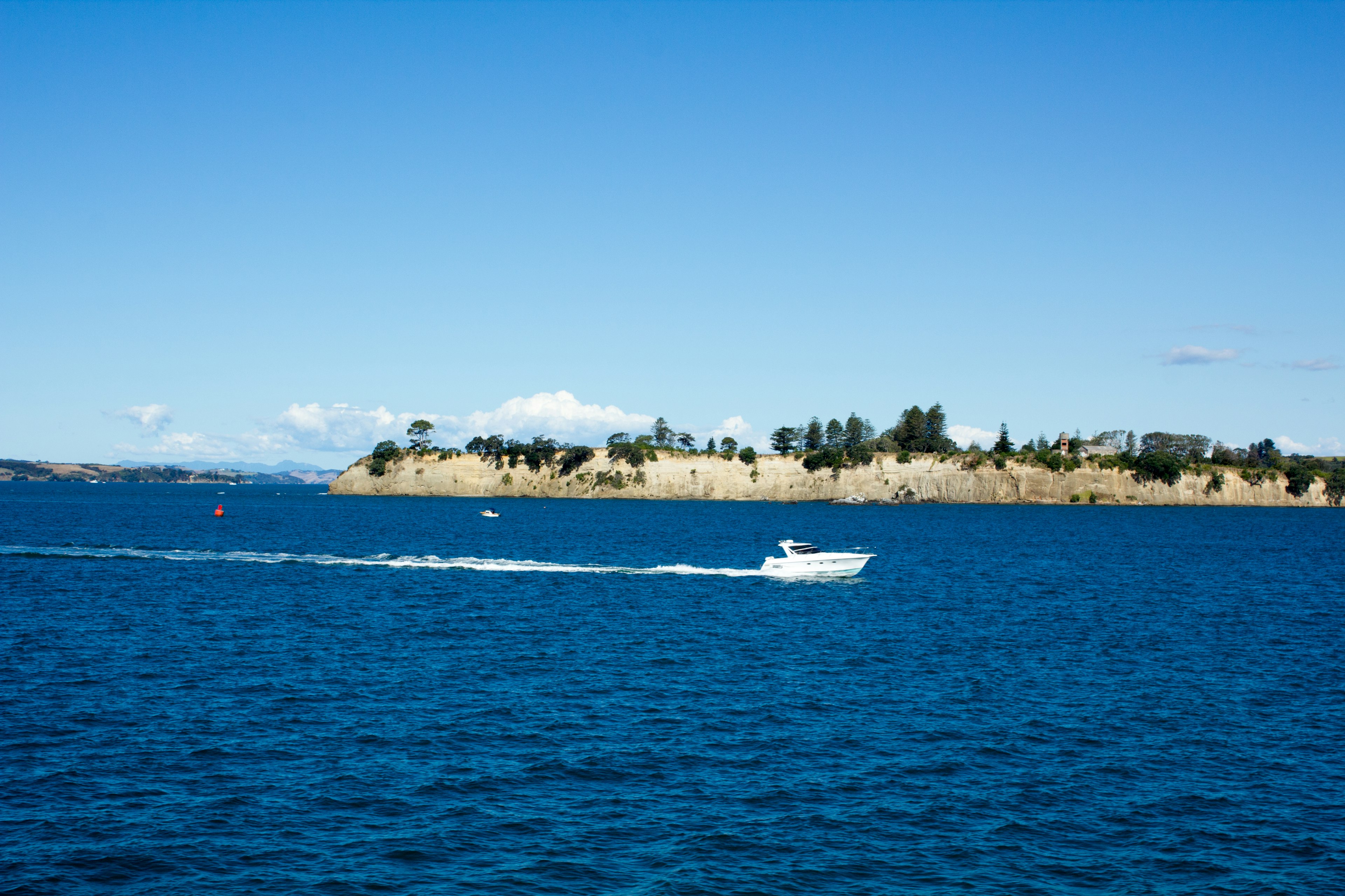 Malersicher Blick auf das blaue Meer mit einem weißen Boot und einer Insel im Hintergrund unter einem klaren blauen Himmel