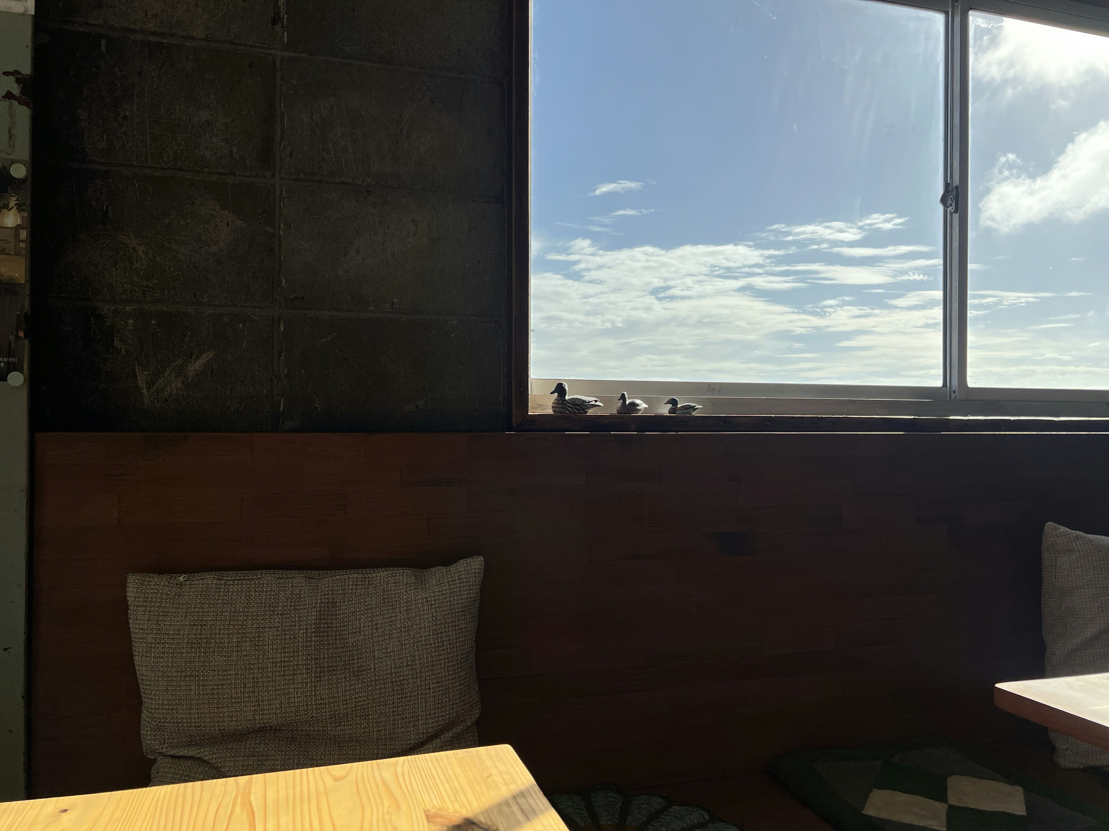 Interior de una cafetería con una ventana brillante que muestra el cielo azul y las nubes