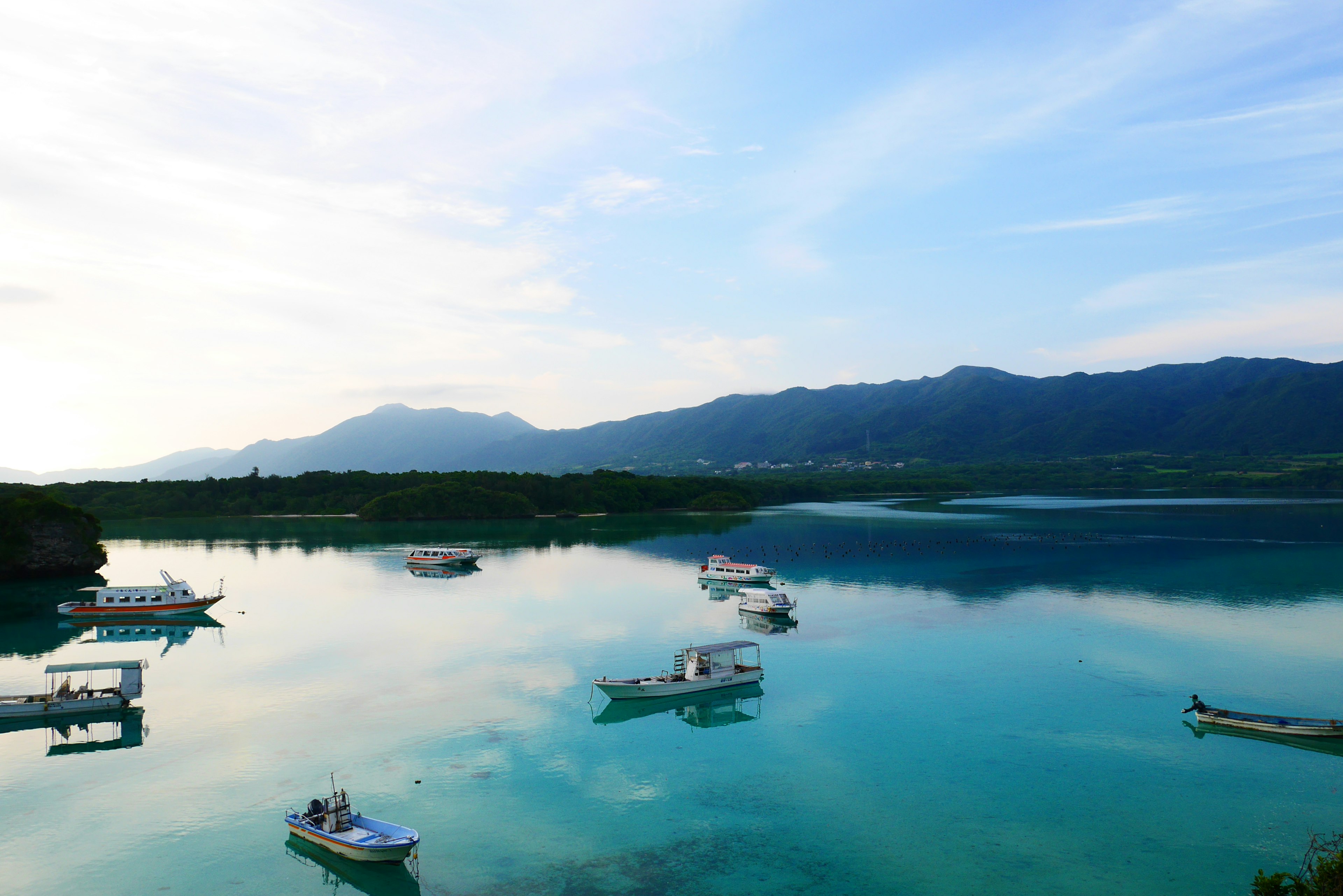 宁静的景色，船只漂浮在平静的水面上，背景是山脉