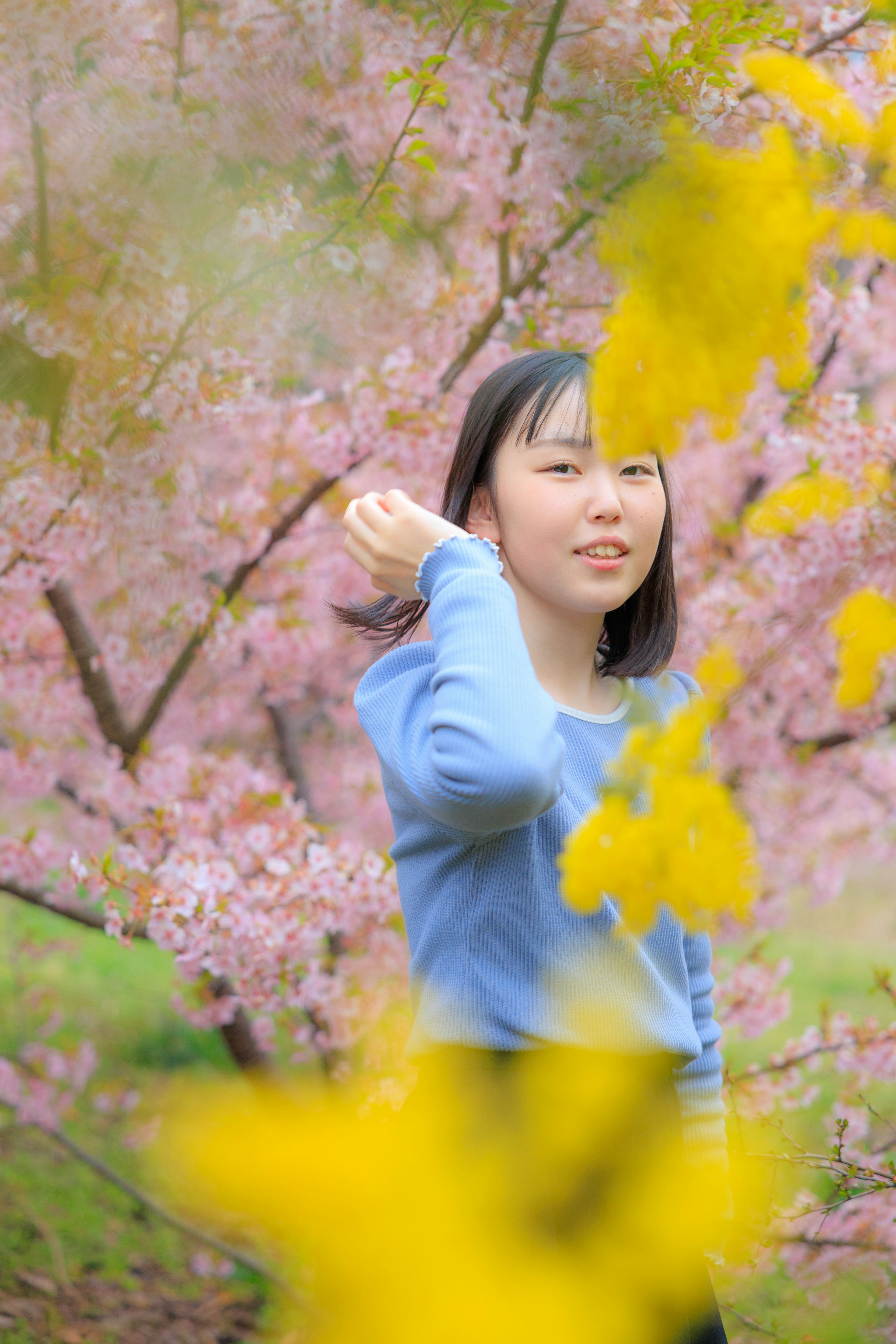 Une jeune femme portant un pull bleu se tient devant des cerisiers en fleurs