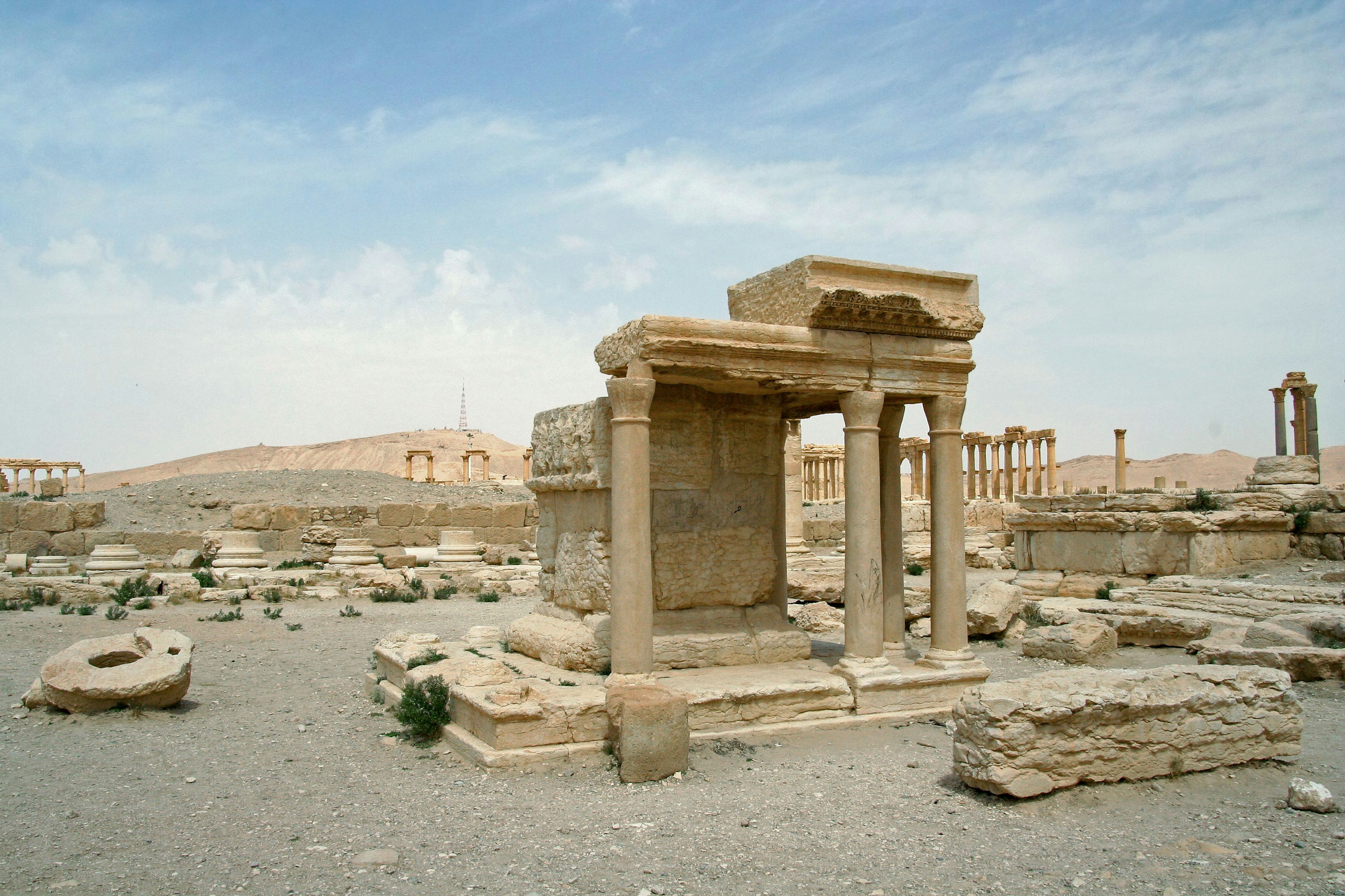 Landscape of ancient ruins featuring a small temple-like structure surrounded by stone debris