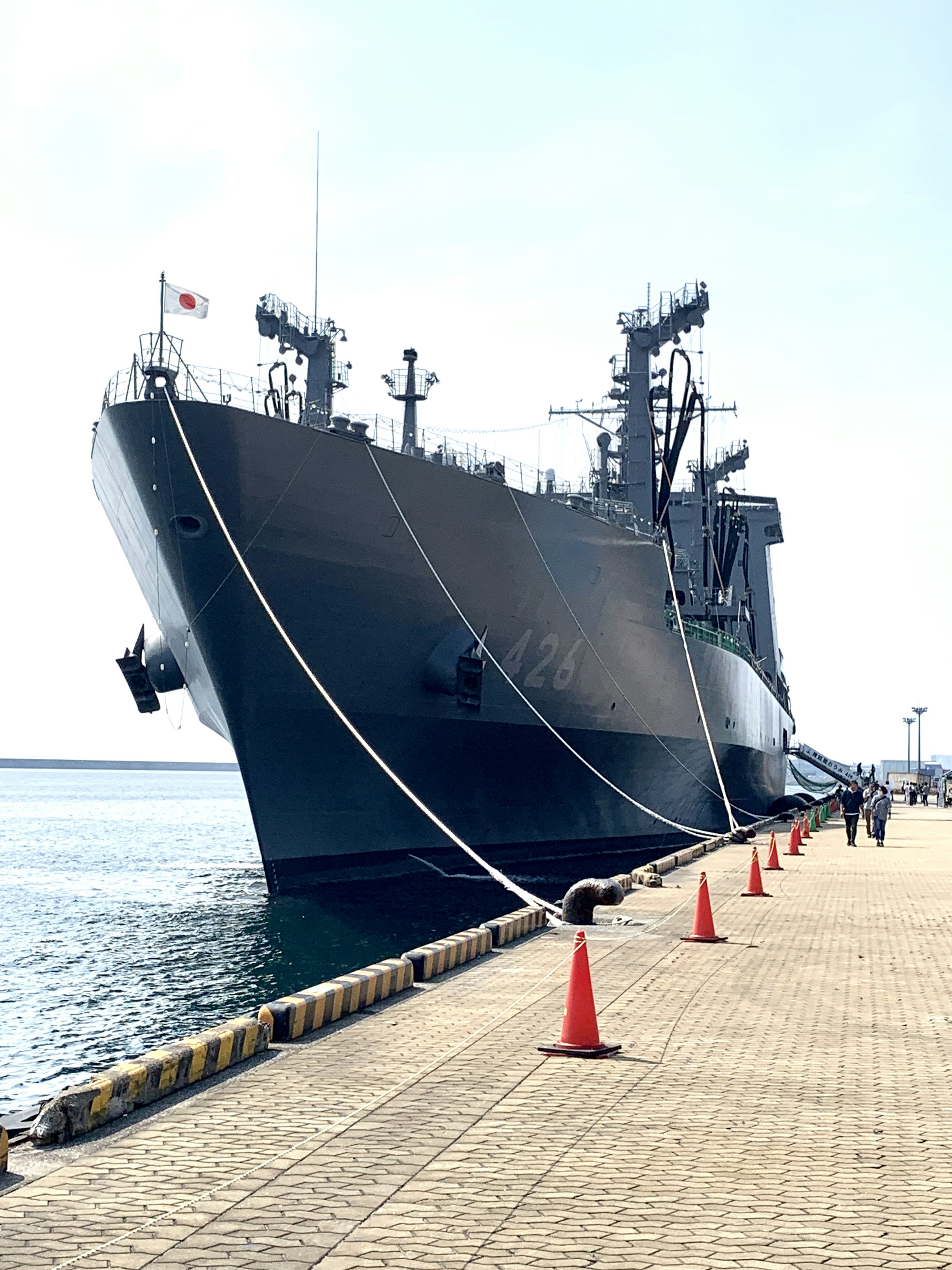 Large black naval ship docked at a port with orange cones