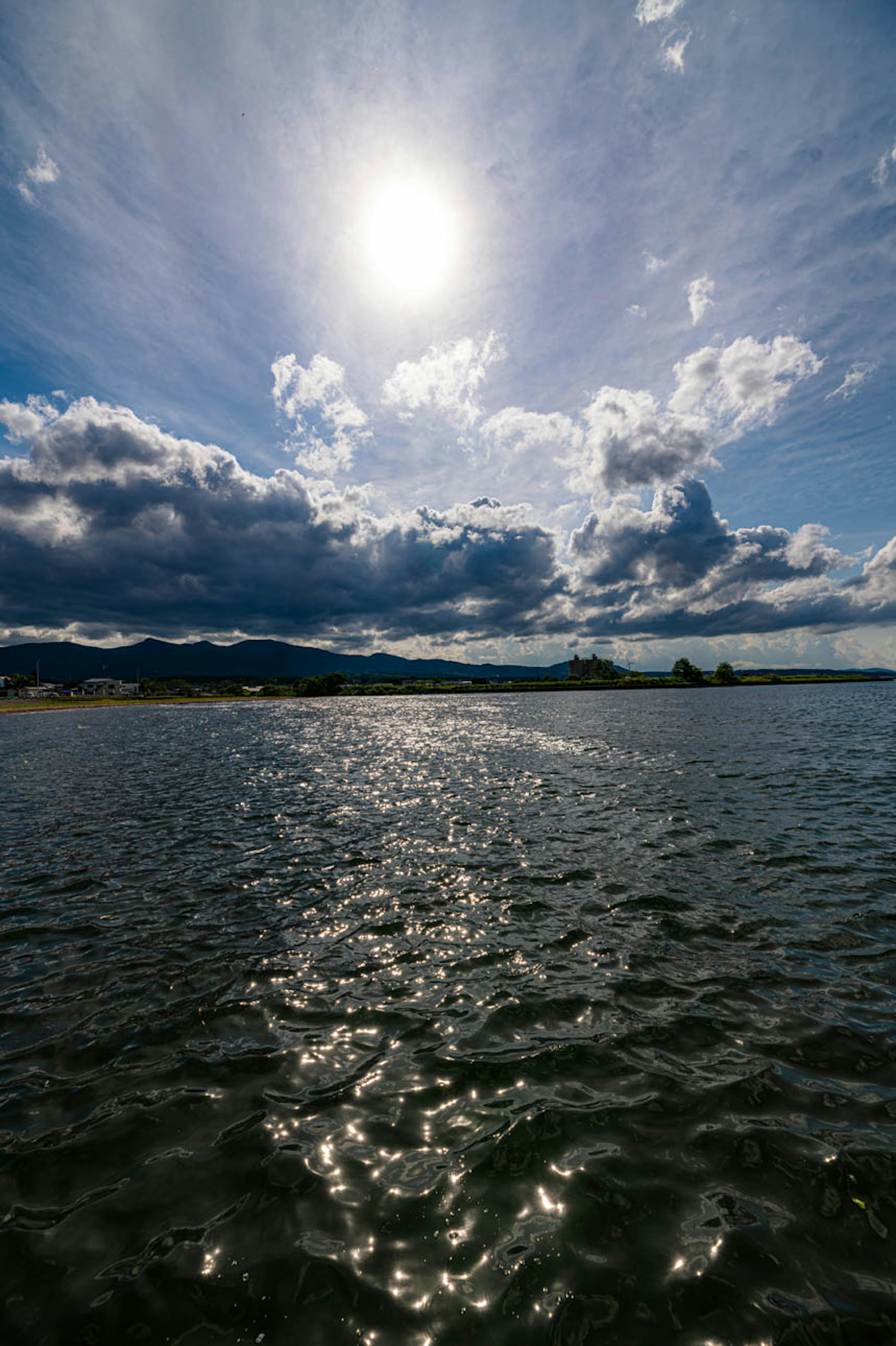 Sole brillante che si riflette sulla superficie dell'acqua con nuvole nel cielo blu