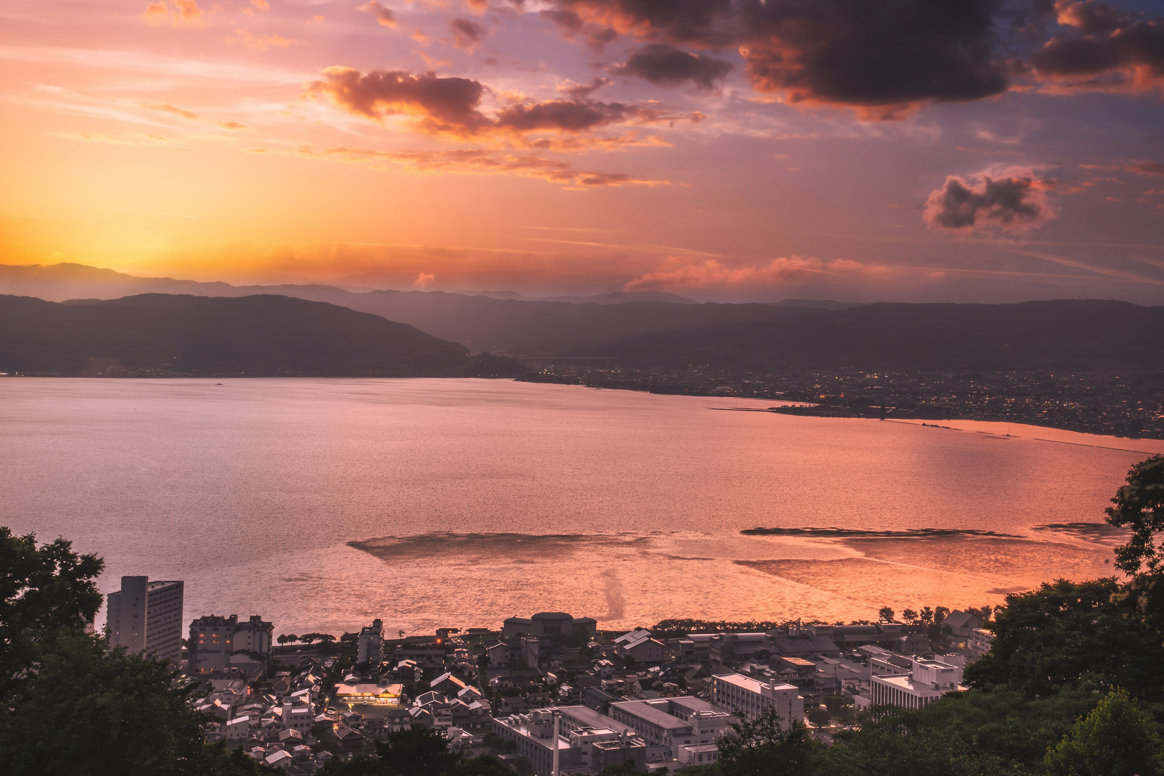 美しい夕焼けと静かな湖の景色で、都市と山々が見える