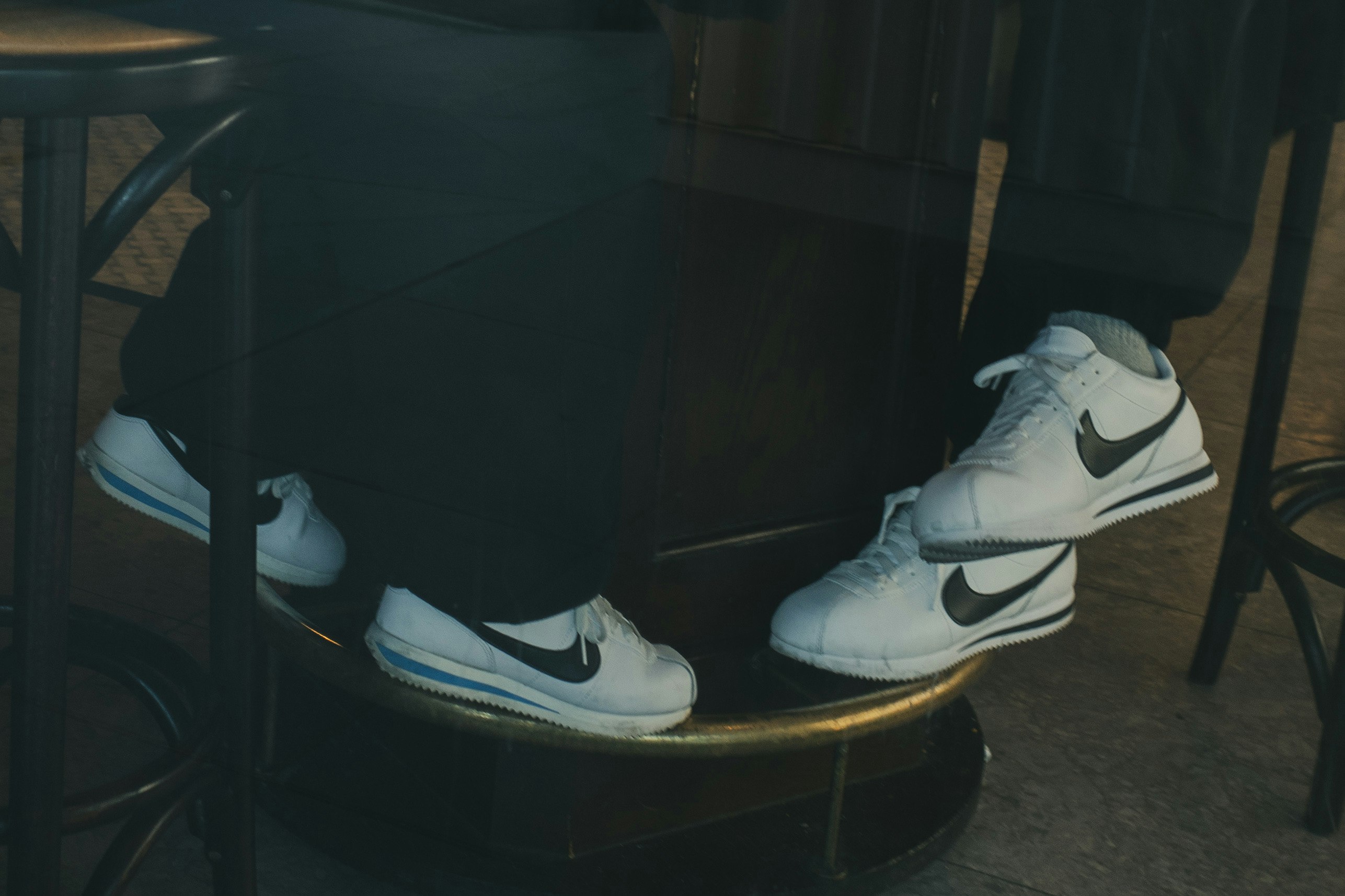 White Nike sneakers on a cafe stool with a person's feet resting