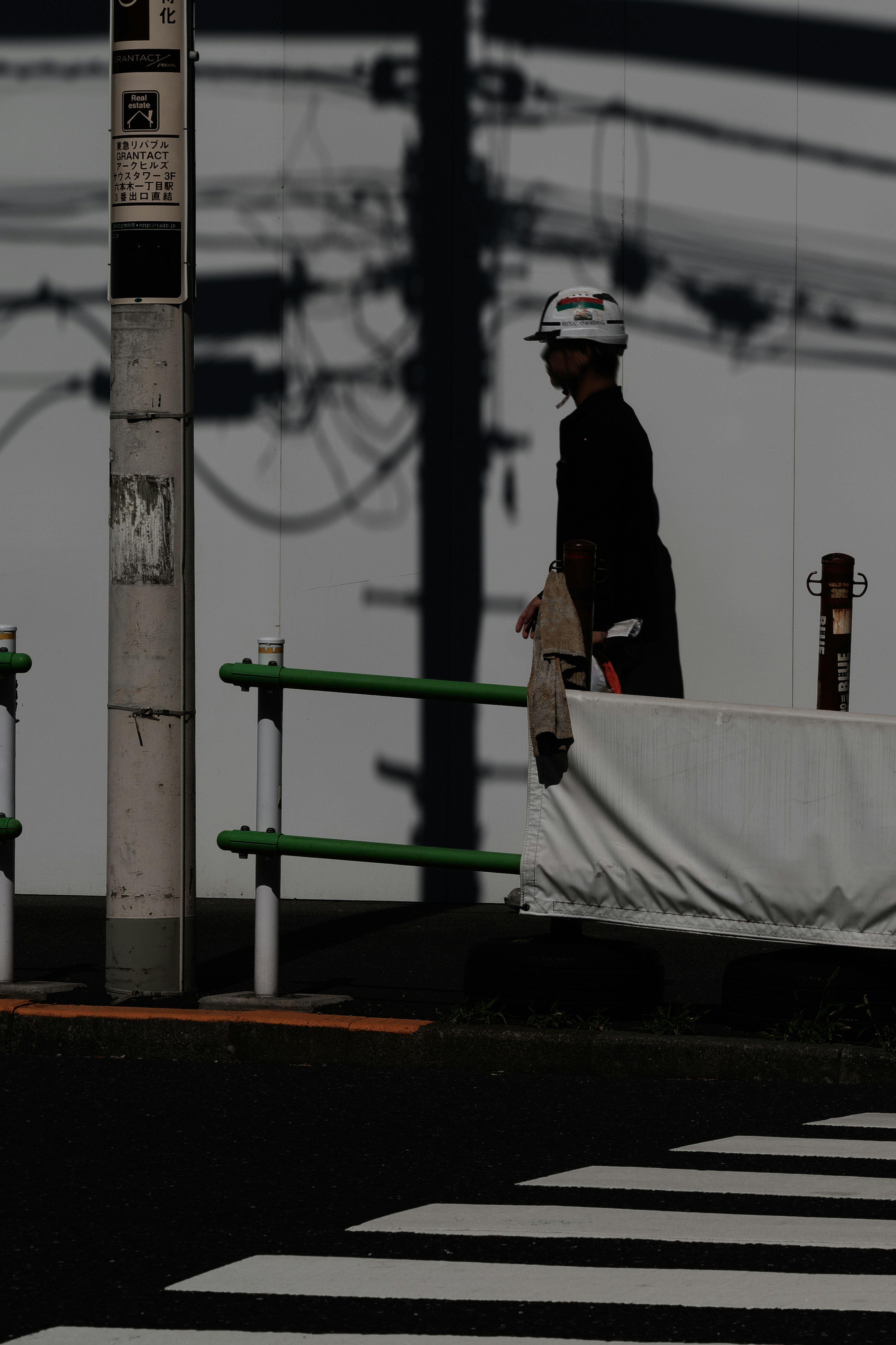 A silhouette of a person walking with a background of power lines and shadows in a city