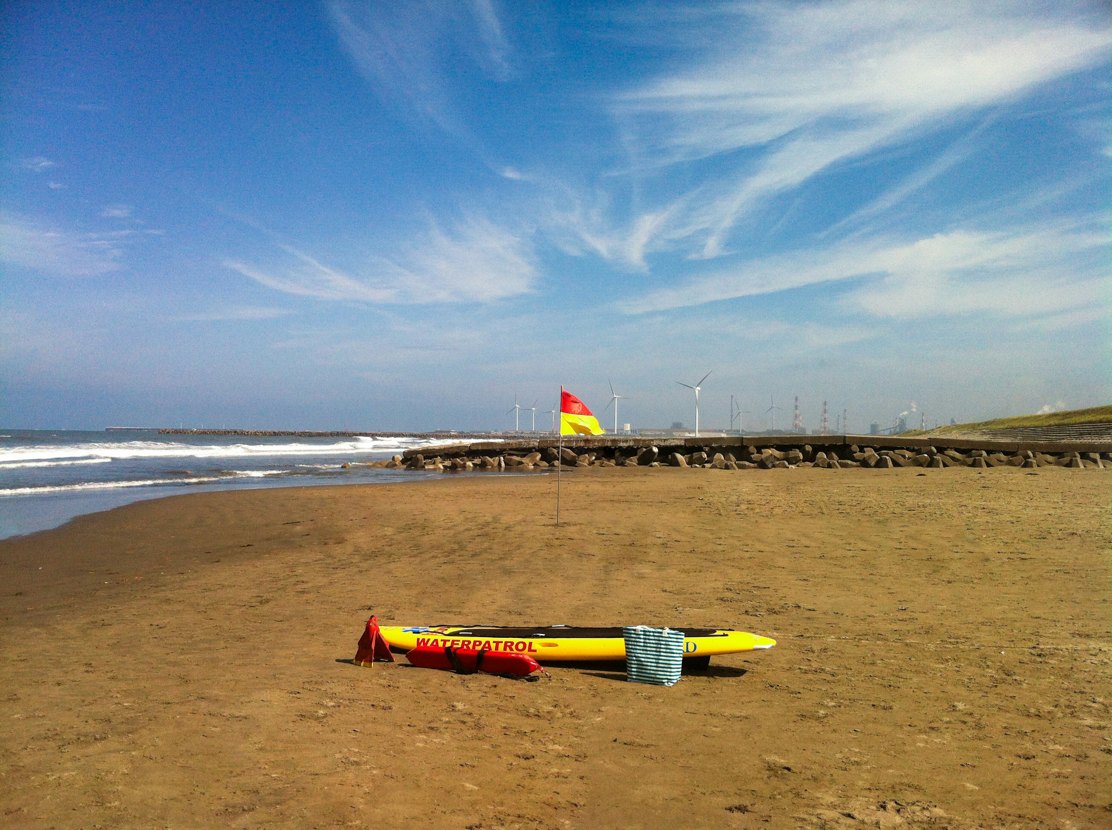 Tavola da surf gialla e boa rossa sulla spiaggia sotto un cielo blu con nuvole bianche