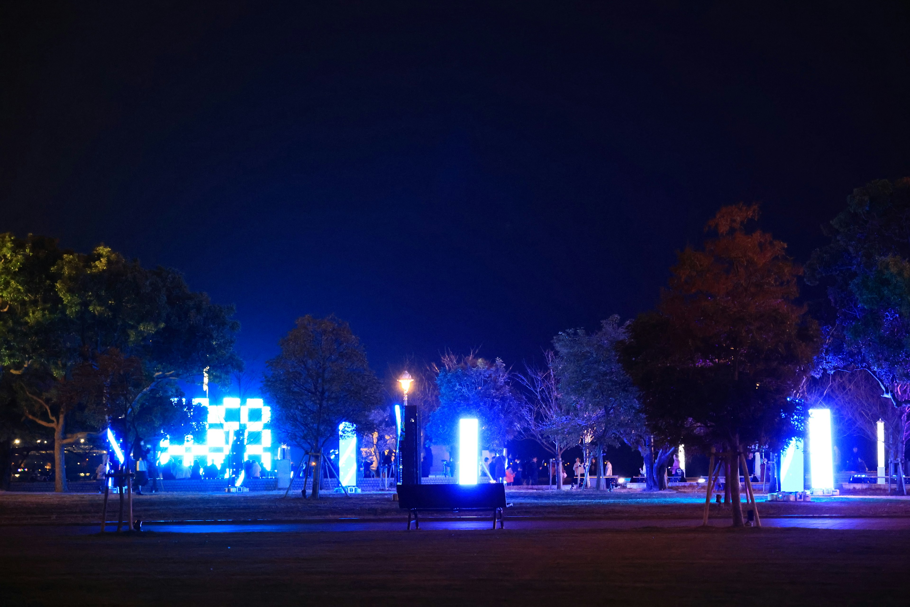 Escena nocturna de parque iluminada por luces azules con árboles y monumentos