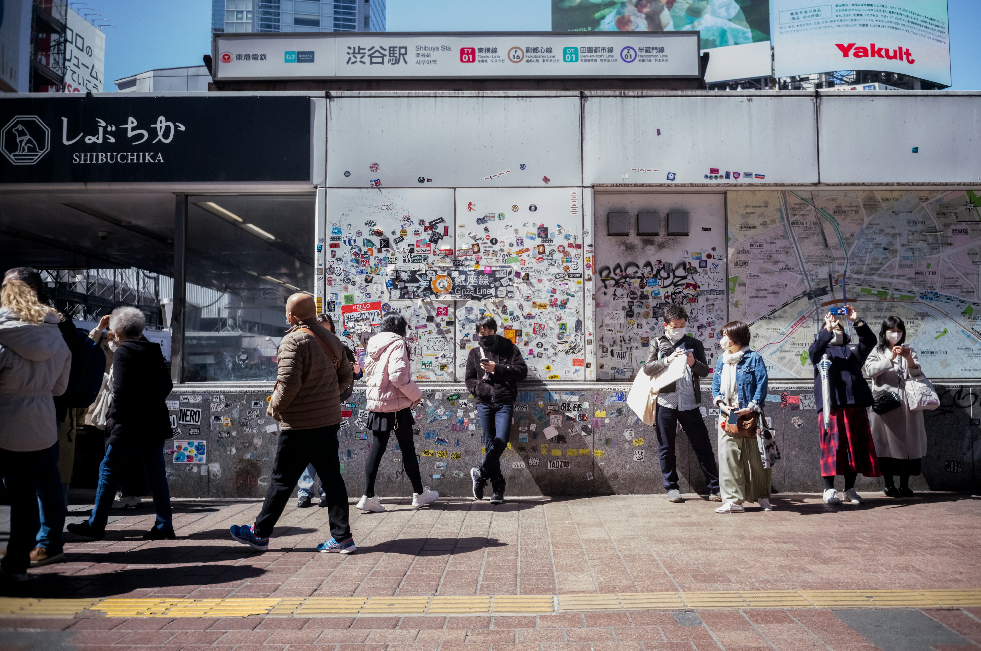 Personas caminando frente a una estación con notas en la pared