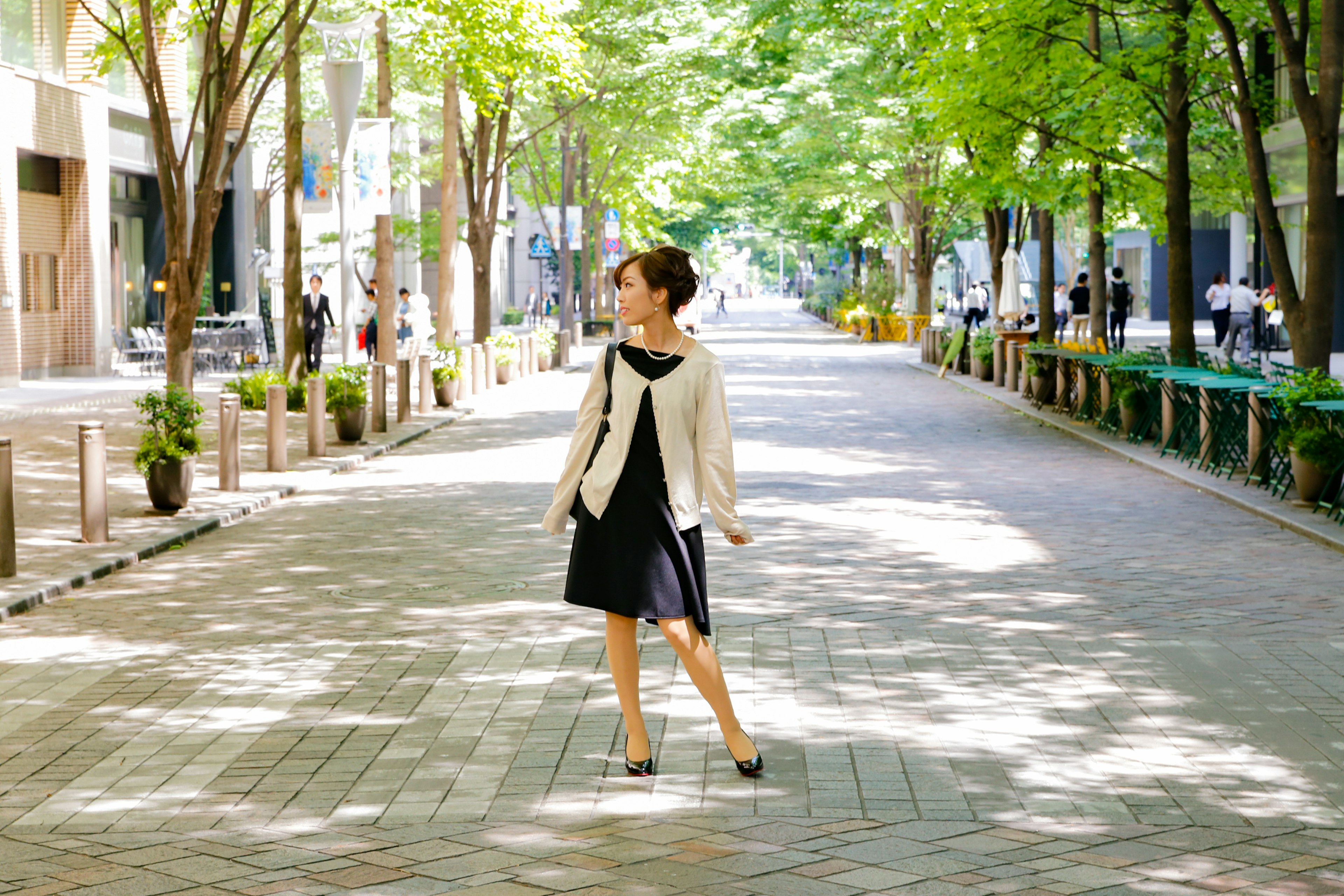 A woman in a black dress standing on a tree-lined street