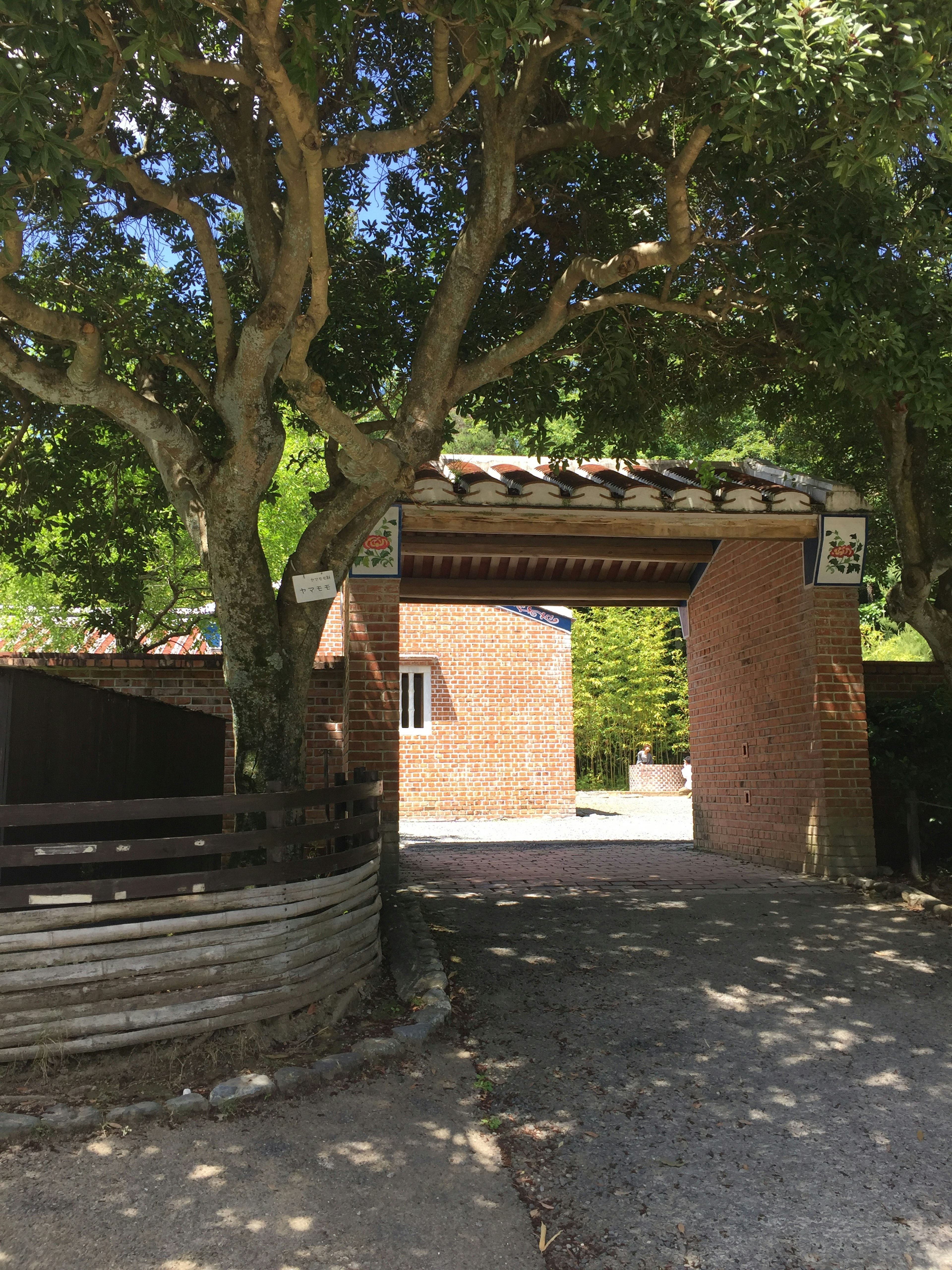 Une entrée rustique avec une porte brune entourée d'arbres verts et d'un chemin de gravier