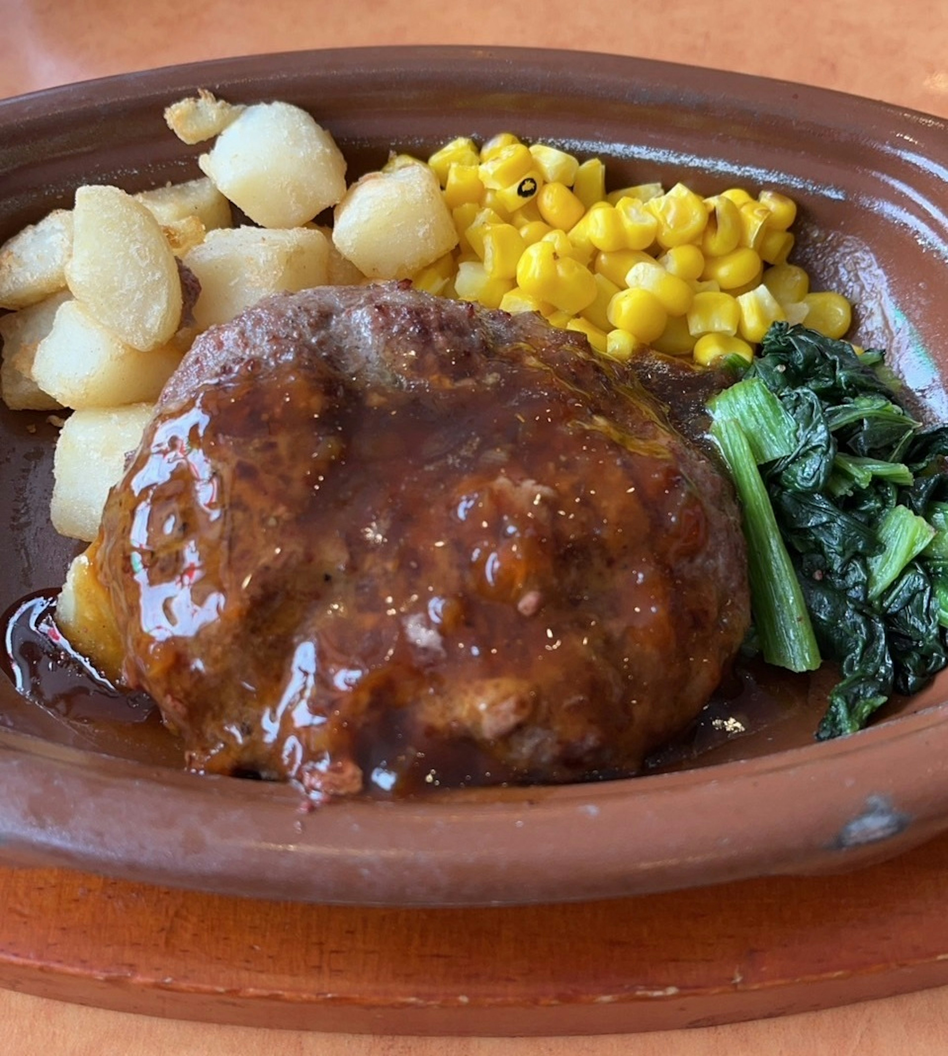 A brown ceramic plate featuring a meat dish with gravy and side vegetables