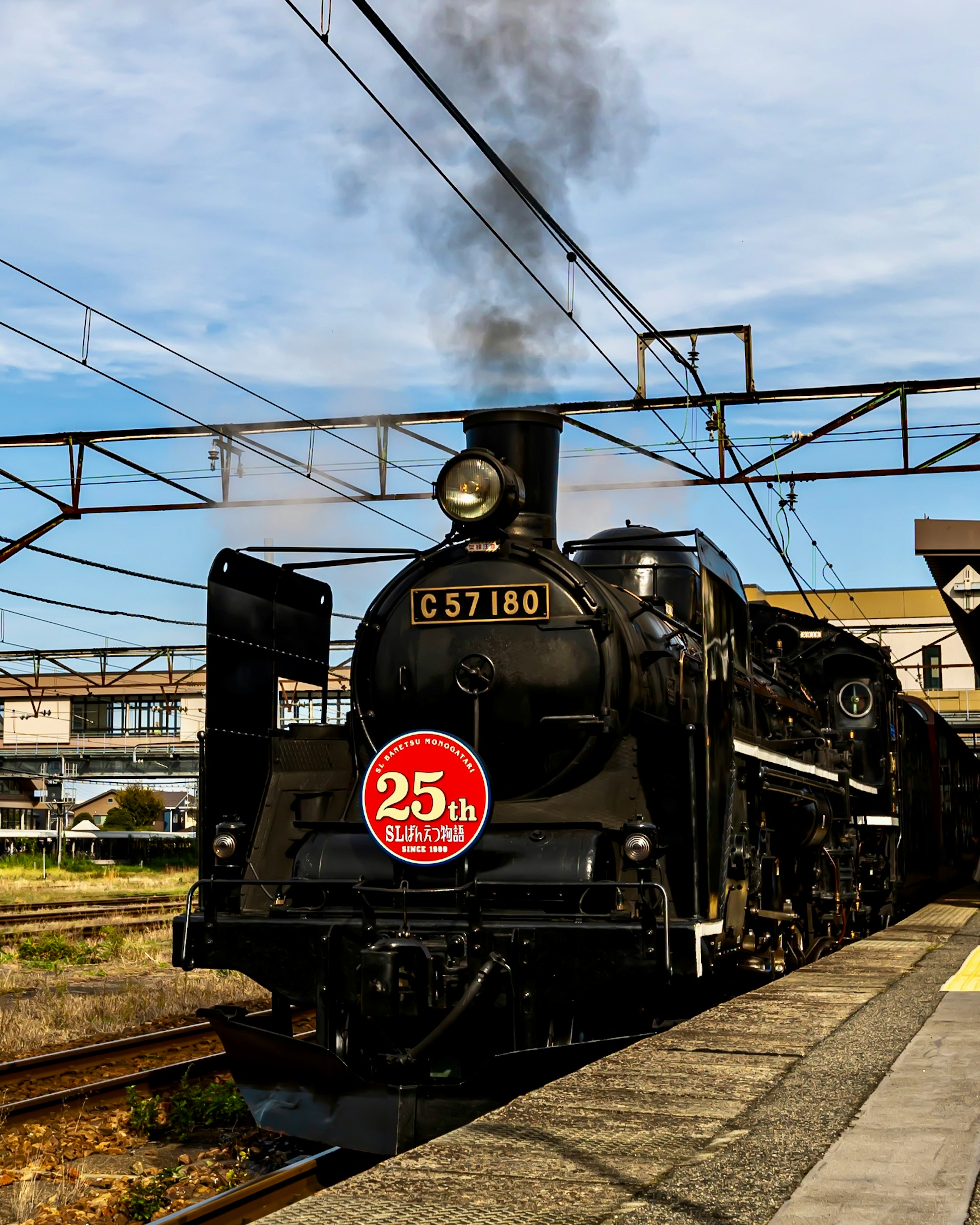 黒い蒸気機関車が駅に停車している様子 25周年の記念プレート