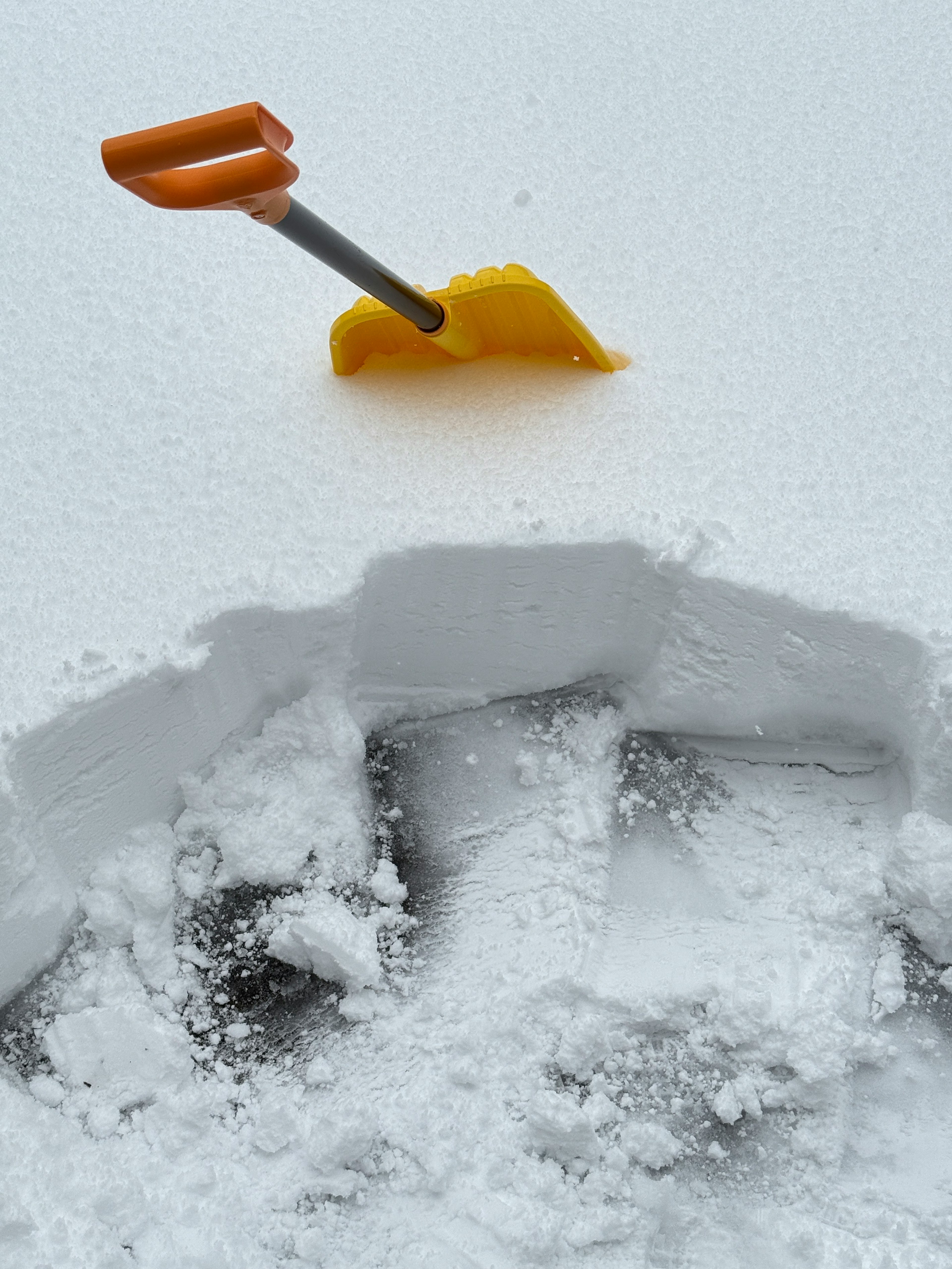 A partially buried shovel in snow with clear footprints around