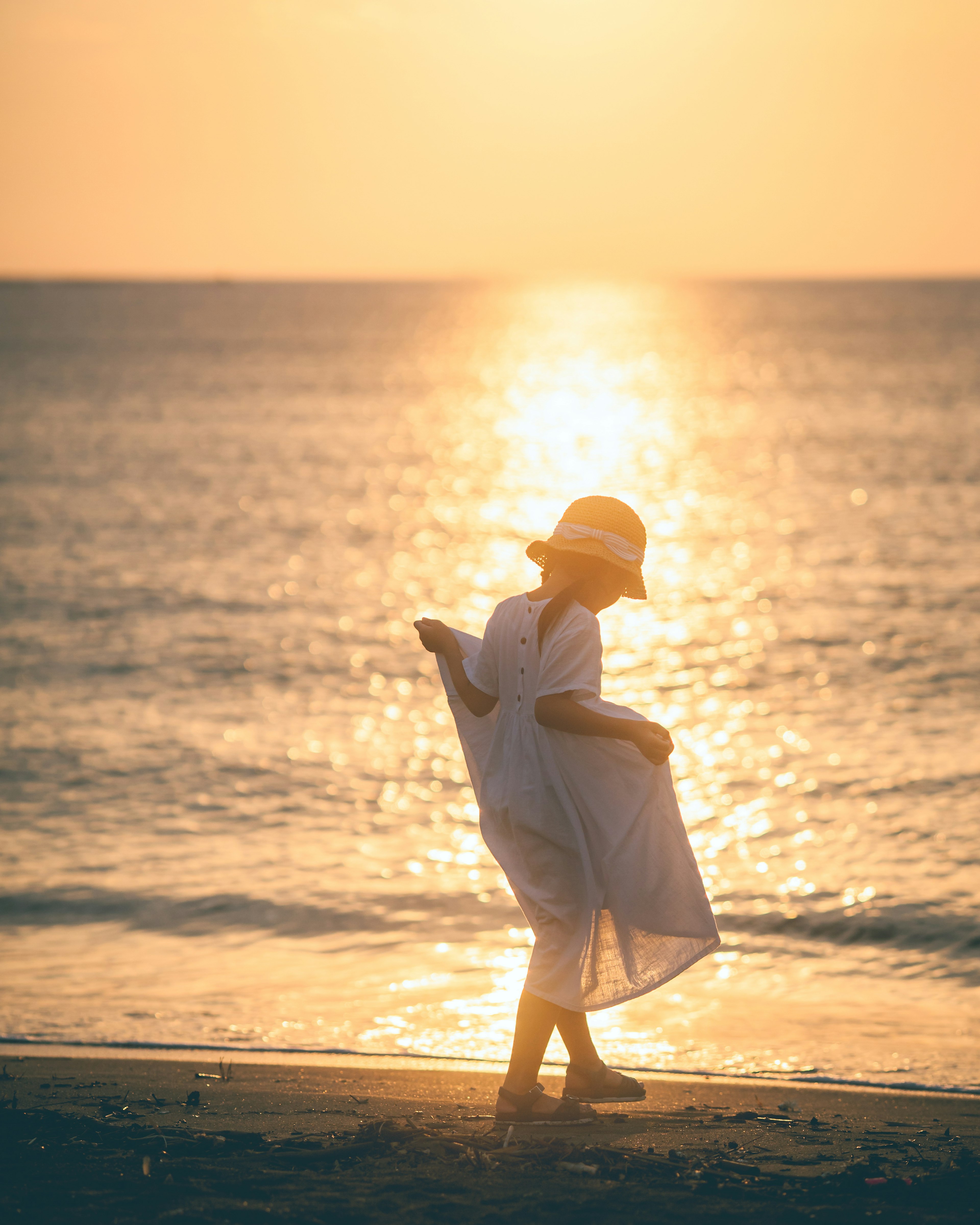 夕日を背にした女性が海辺を歩いているシーン