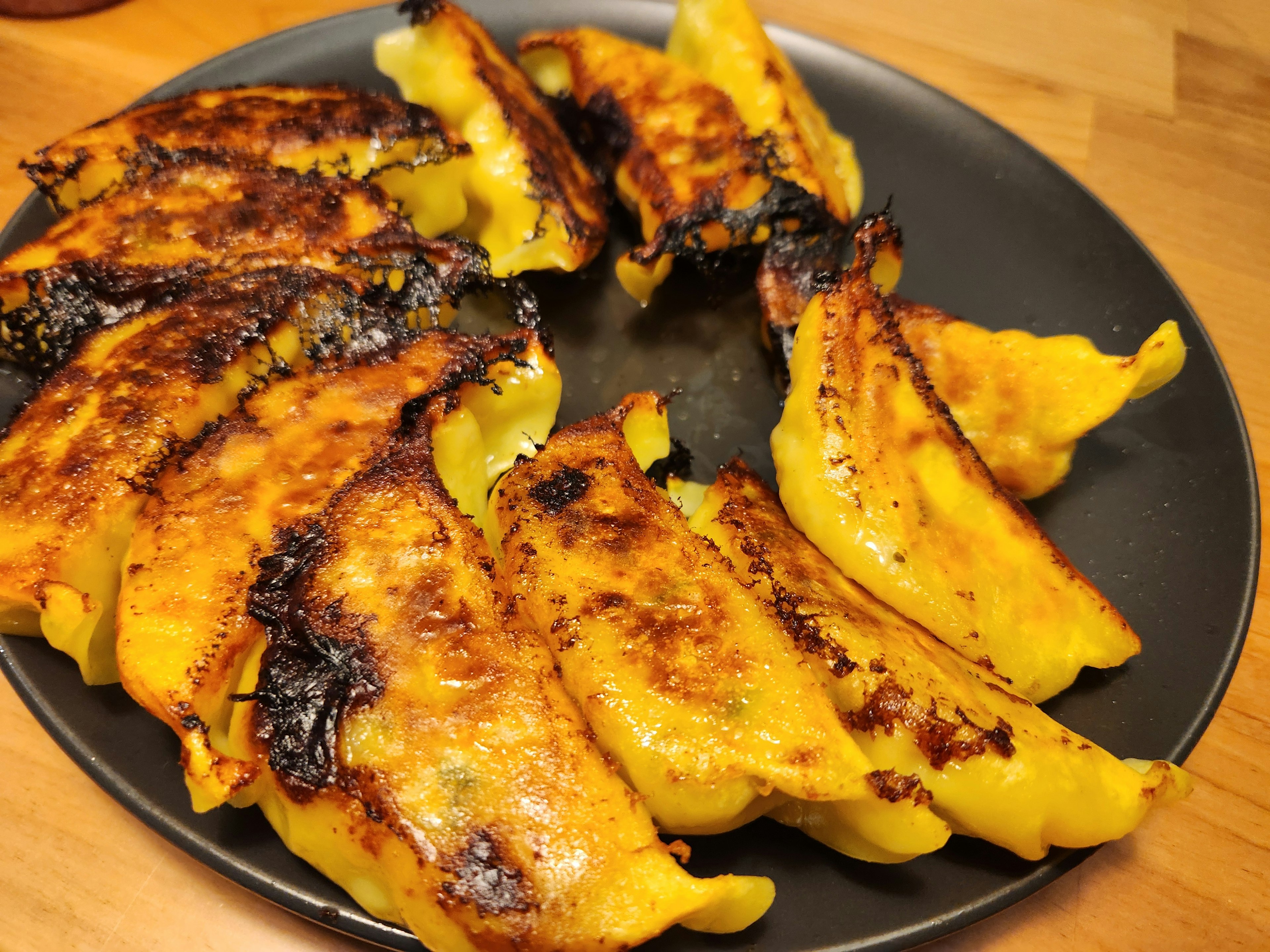 Gyoza frits avec bords croustillants disposés sur une assiette noire