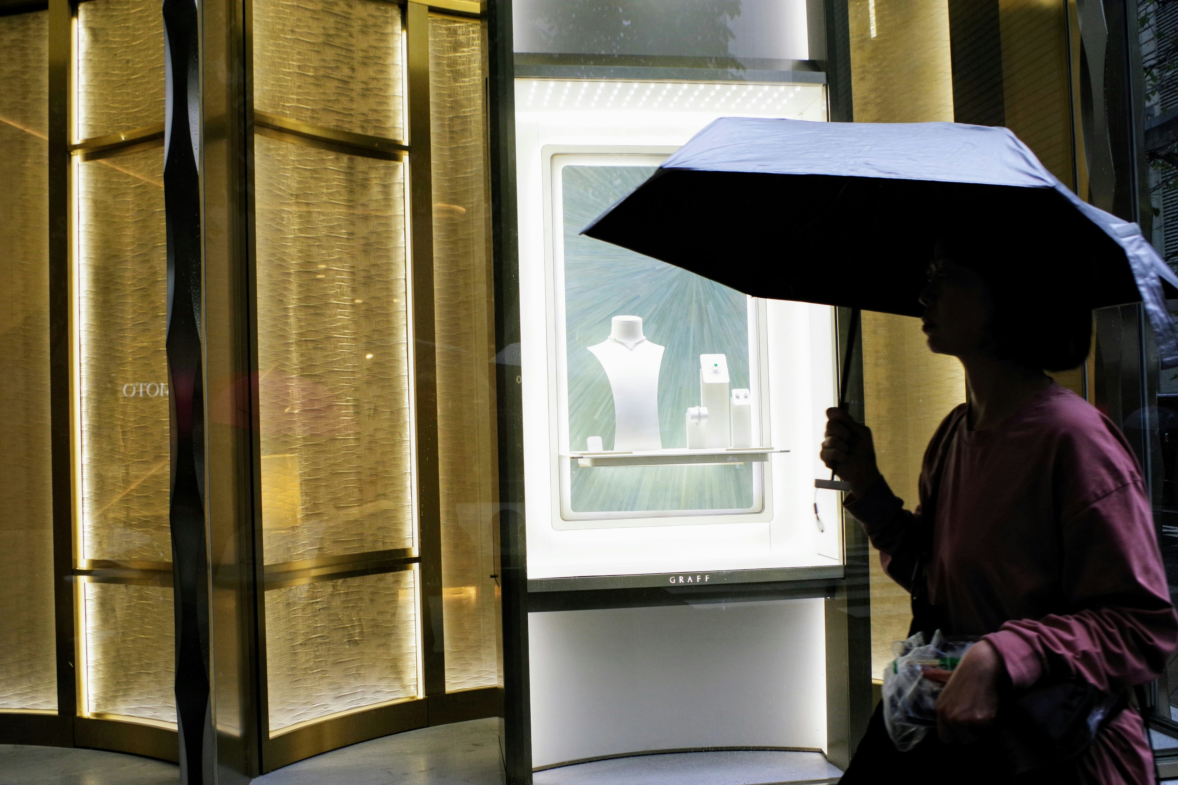 A person with an umbrella passing by a jewelry store window display