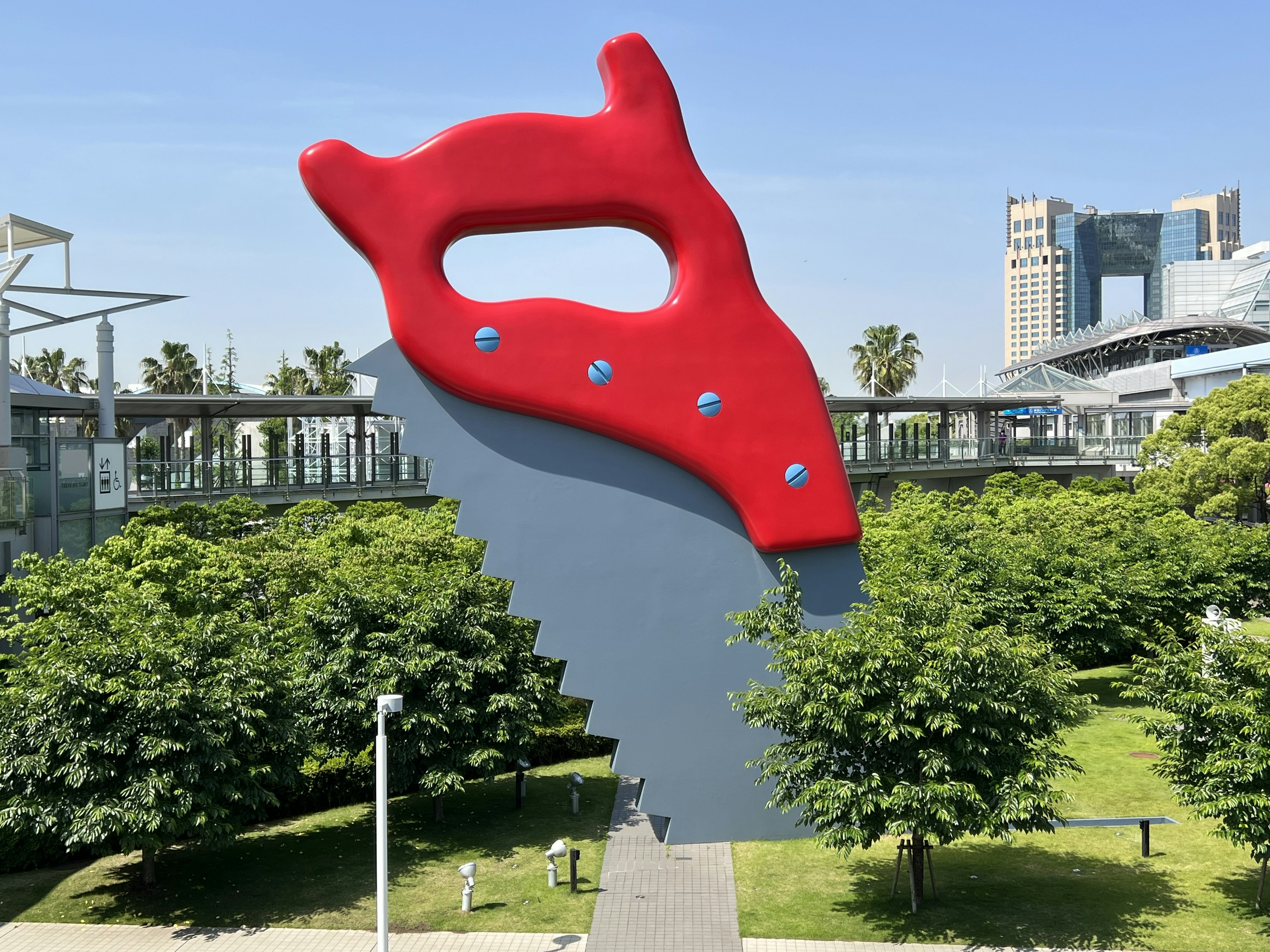 Giant red saw sculpture in a park surrounded by green trees