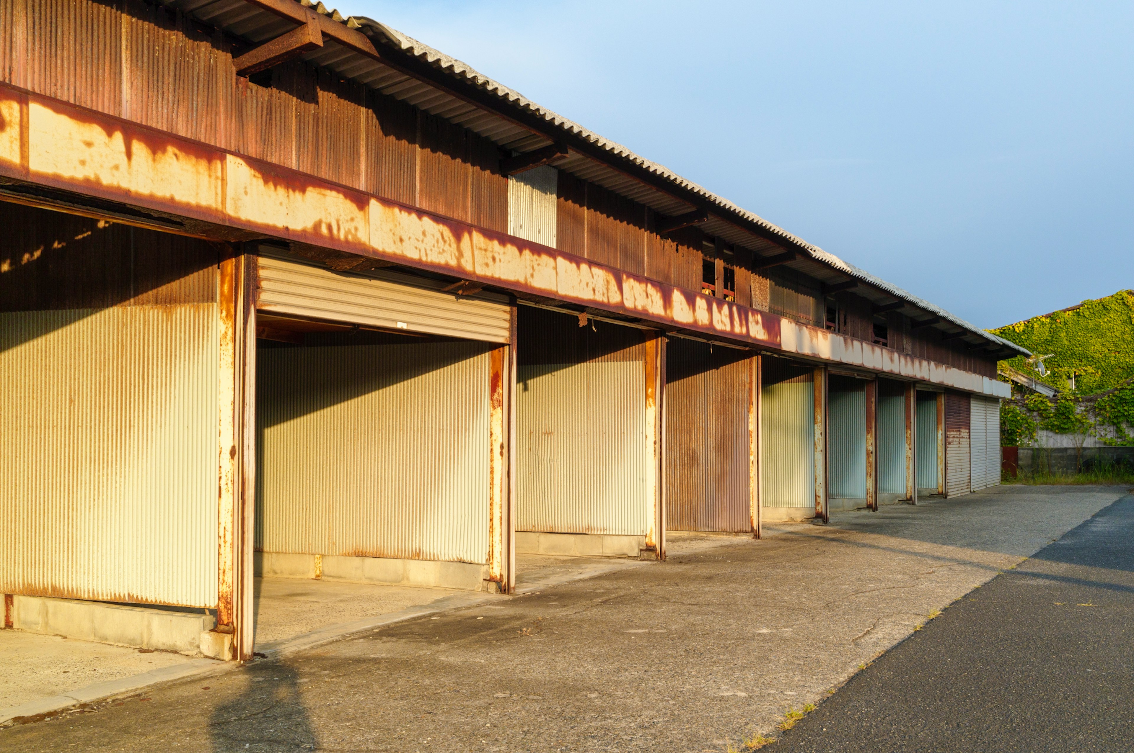 Extérieur d'un ancien entrepôt avec des murs en métal rouillé et plusieurs portes de garage vides