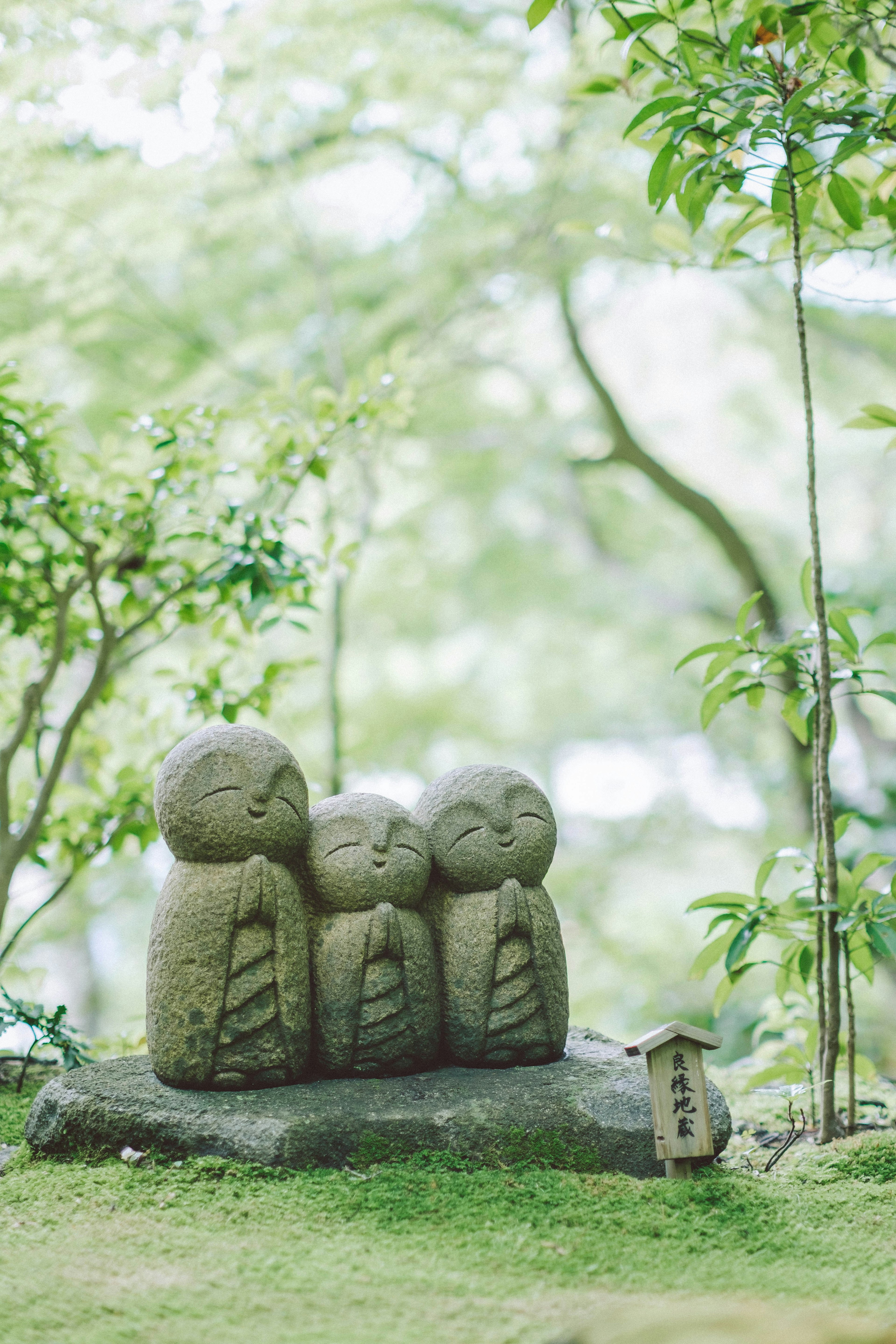 Trois statues en pierre avec des expressions minimales entourées de verdure